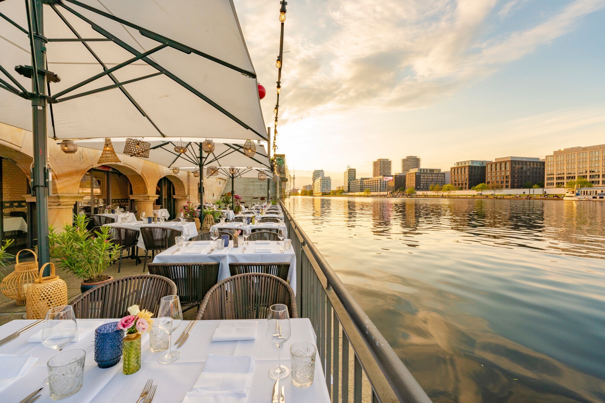 Weiß eingedeckte Tische auf der Terrasse eines eleganten Restaurants am Wasser in Berlin.