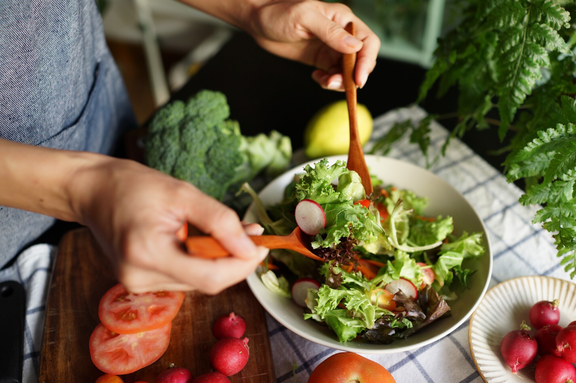 Frau mischt einen Salat in einer Schüssel, drumherum liegt weiteres Gemüse.