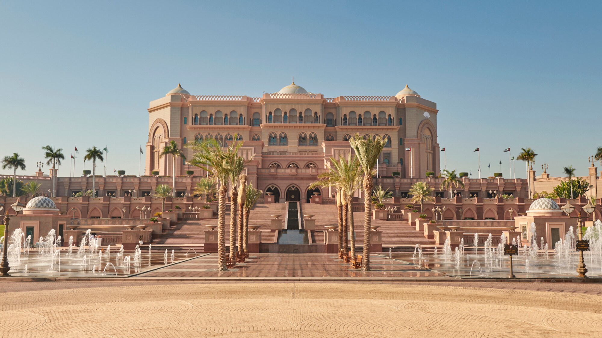 Außenansicht des Emirates Palace Mandarin Oriental Hotels in Abu Dhabi mit Palmen und Brunnen im Vordergrund.