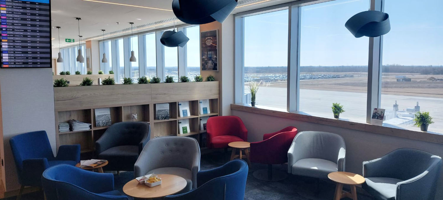 Flughafen-Lounge mit Sitzgruppen und Blick aufs Rollfeld.