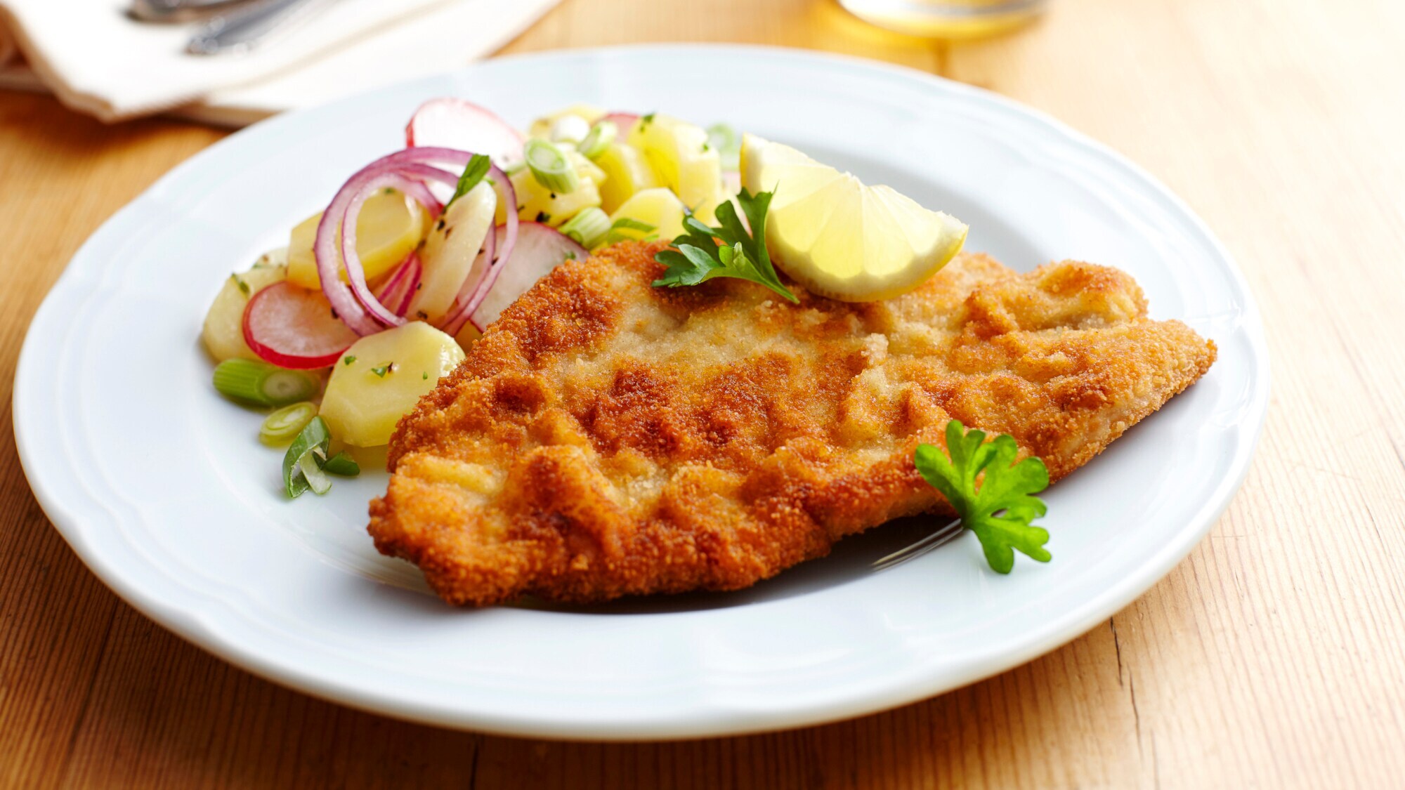 Ein paniertes Schnitzel mit Kartoffelsalat auf einem weißen Teller. Ein paniertes Schnitzel mit Kartoffelsalat auf einem weißen Teller.