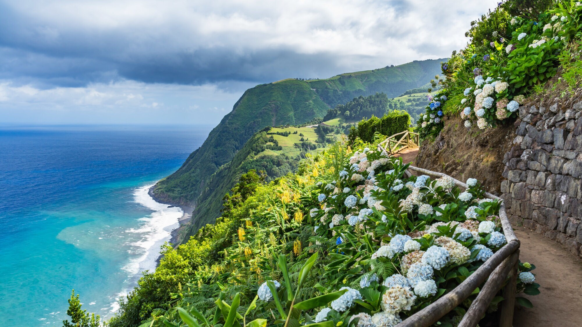 Mit Hortensien bewachsener Küstenweg auf der Azoreninsel São Miguel mit Blick auf den Atlantik.