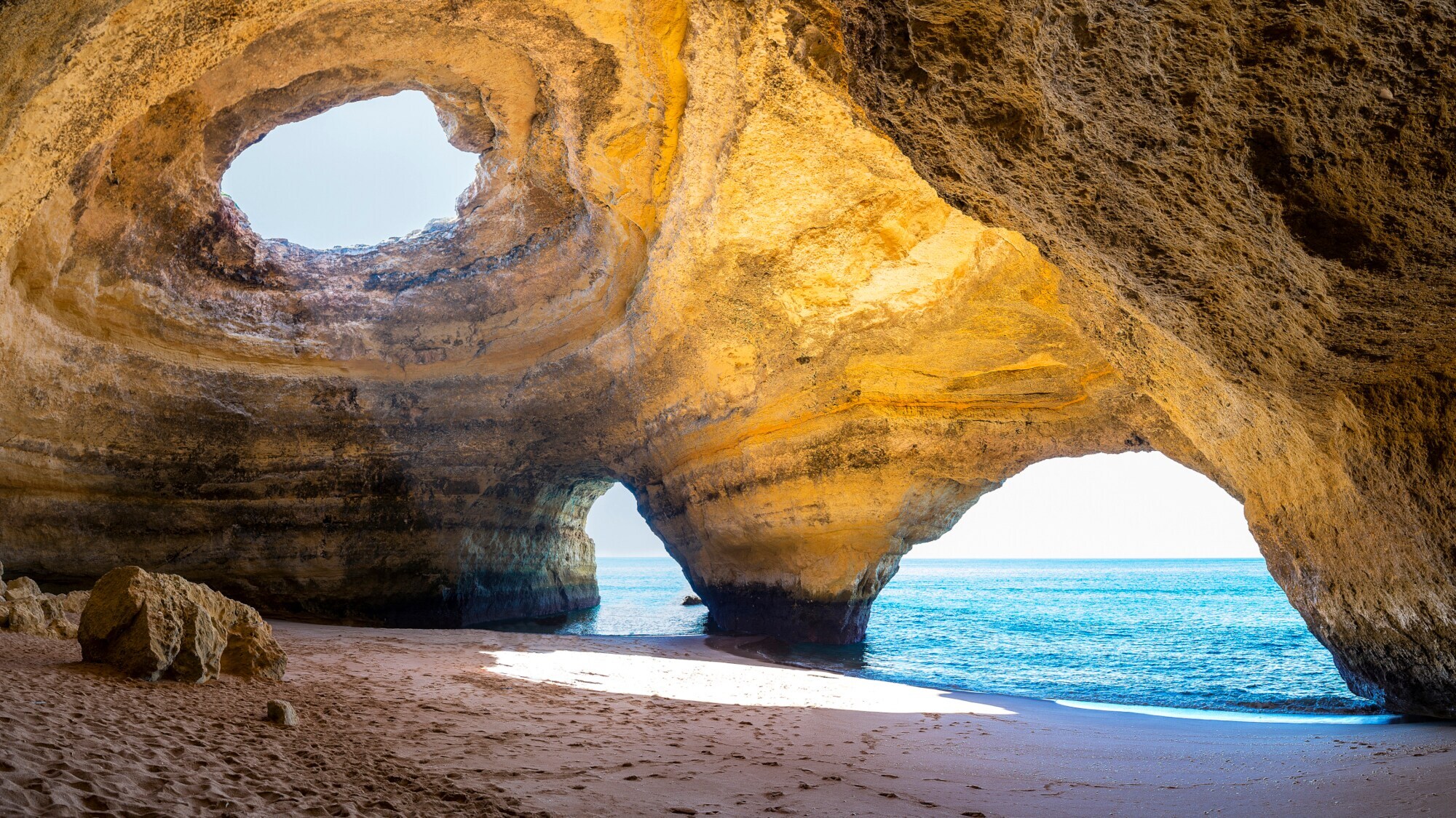 Innenraum der Meereshöhle Algar de Benagil an der Algarve, in dessen Decke ein Loch im Gestein ist, durch das die Sonne scheint.