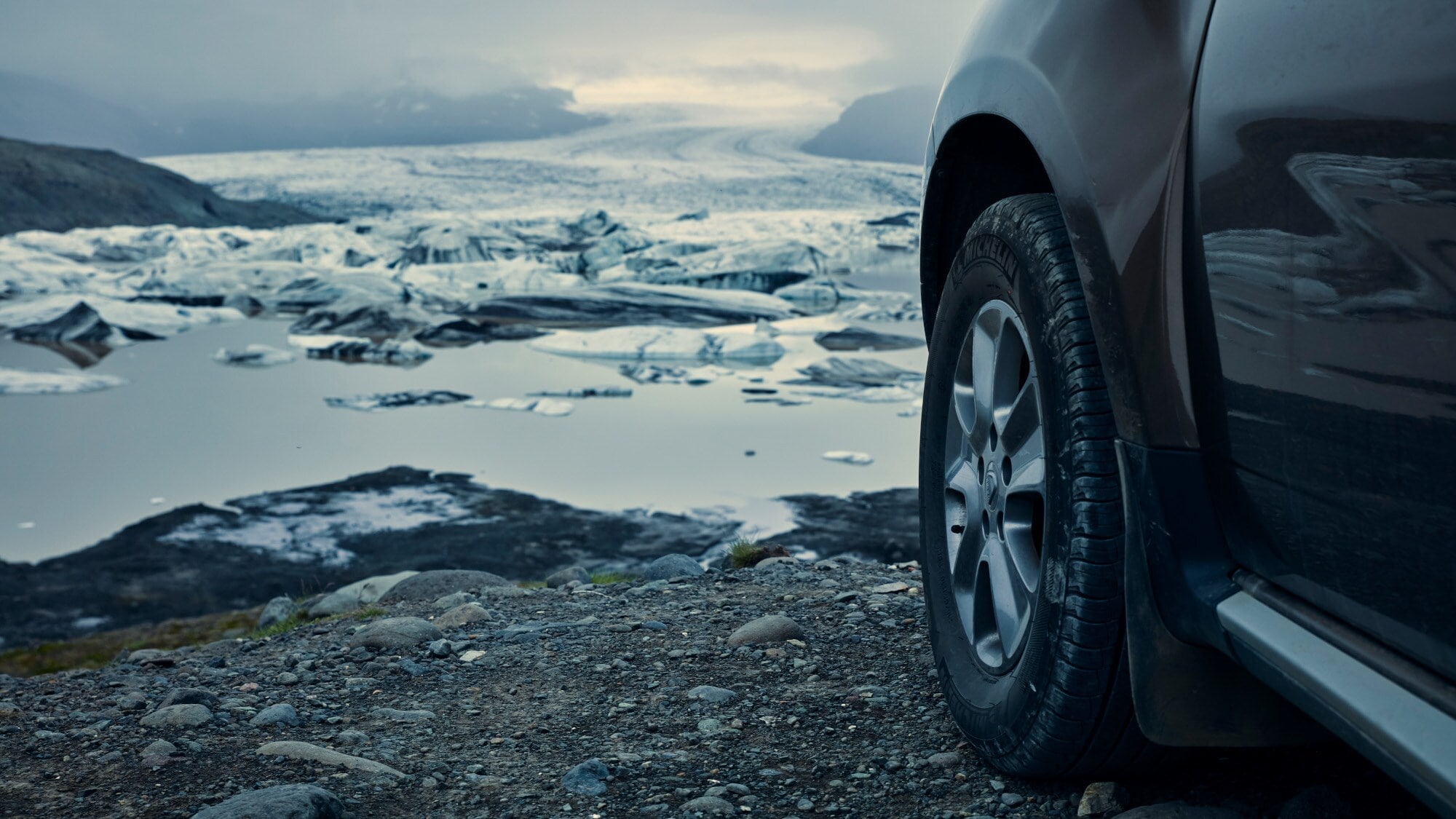Nahaufnahme eines Vorderreifens an einem dunklen Auto in einer Gletscherlandschaft. Nahaufnahme eines Vorderreifens an einem dunklen Auto in einer Gletscherlandschaft.