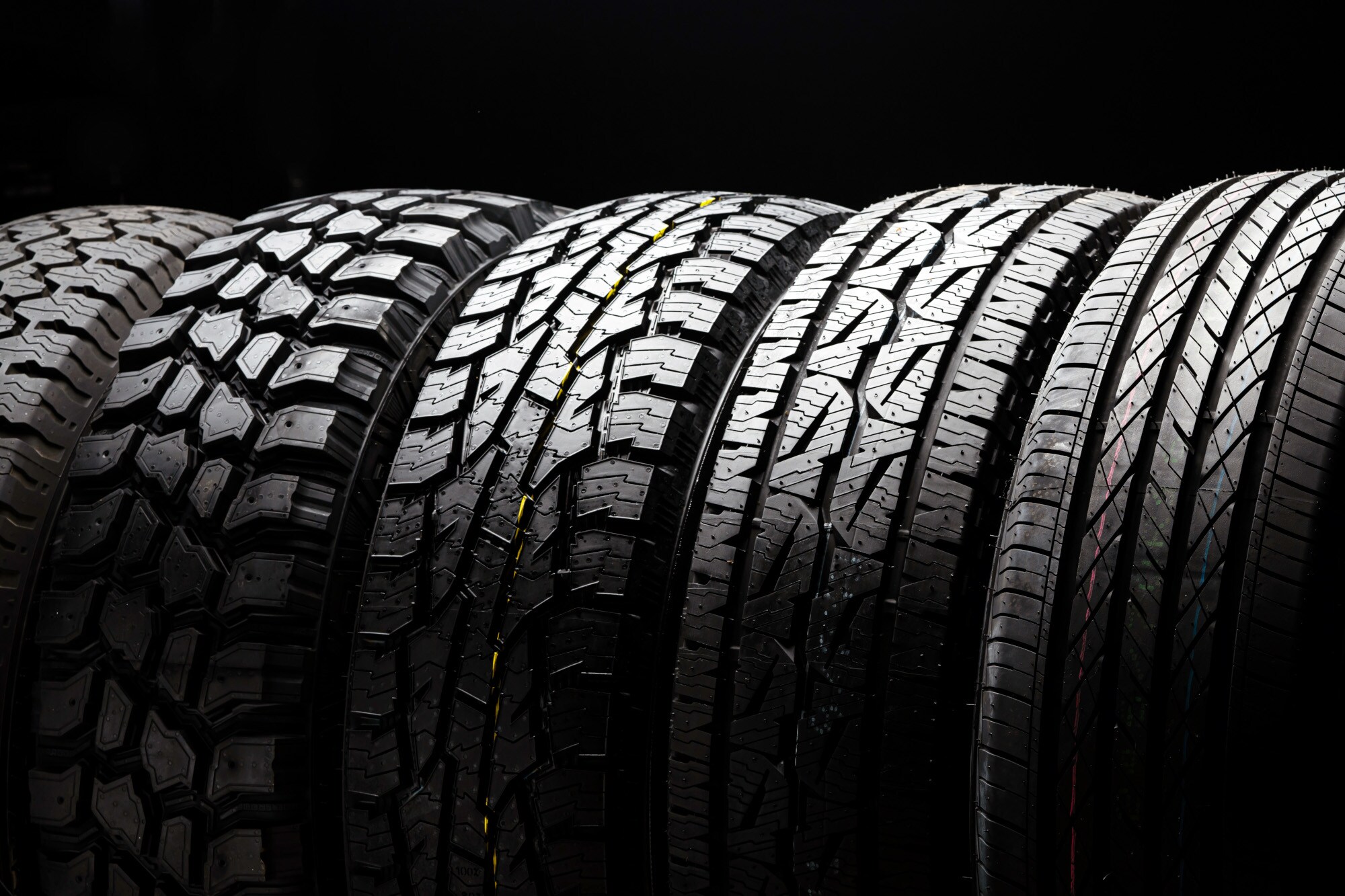 Fünf 4x4-Autoreifen nebeneinander, mit ausgeleuchtetem Profil vor schwarzem Hintergrund.