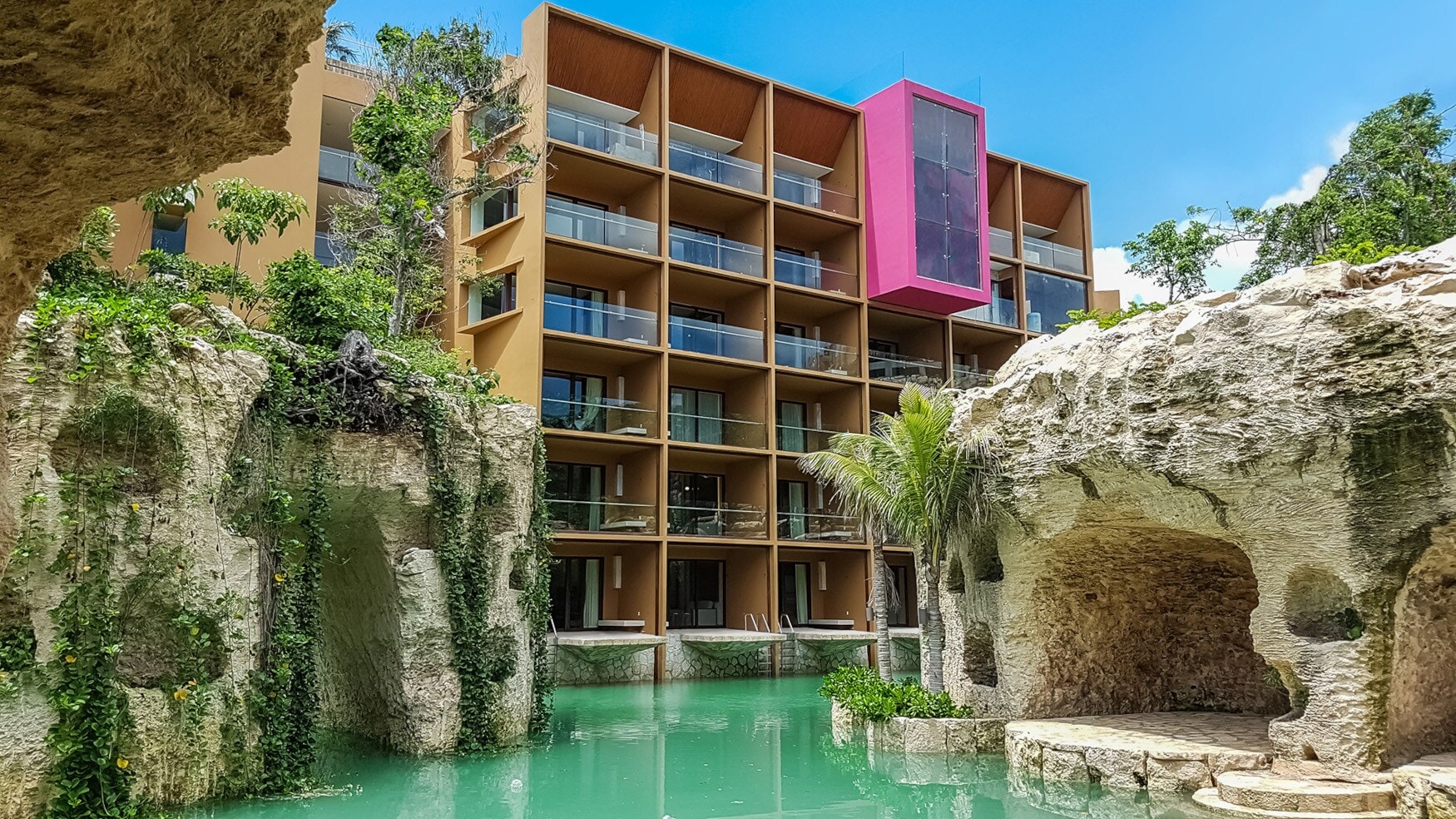 Moderner Hotelkomplex, umgeben von bepflanzten Felsen an einem Pool mit türkisfarbenem Wasser. Moderner Hotelkomplex, umgeben von bepflanzten Felsen an einem Pool mit türkisfarbenem Wasser.