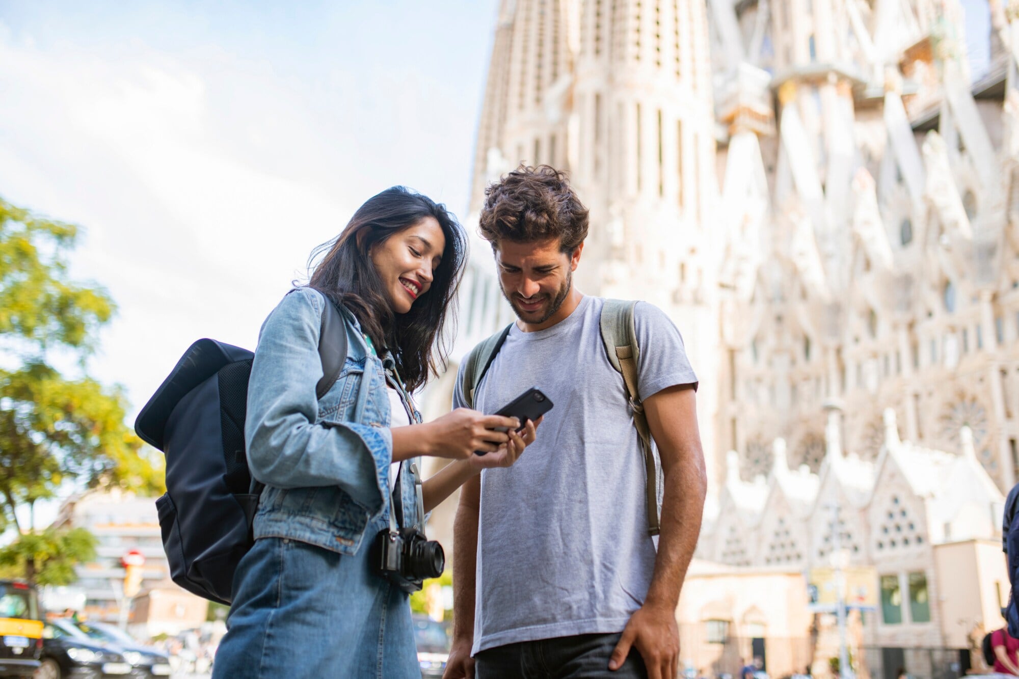 Zwei Personen stehen in Barcelona vor der Sagrada Família und blicken zusammen auf ein Smartphone. Zwei Personen stehen in Barcelona vor der Sagrada Família und blicken zusammen auf ein Smartphone.
