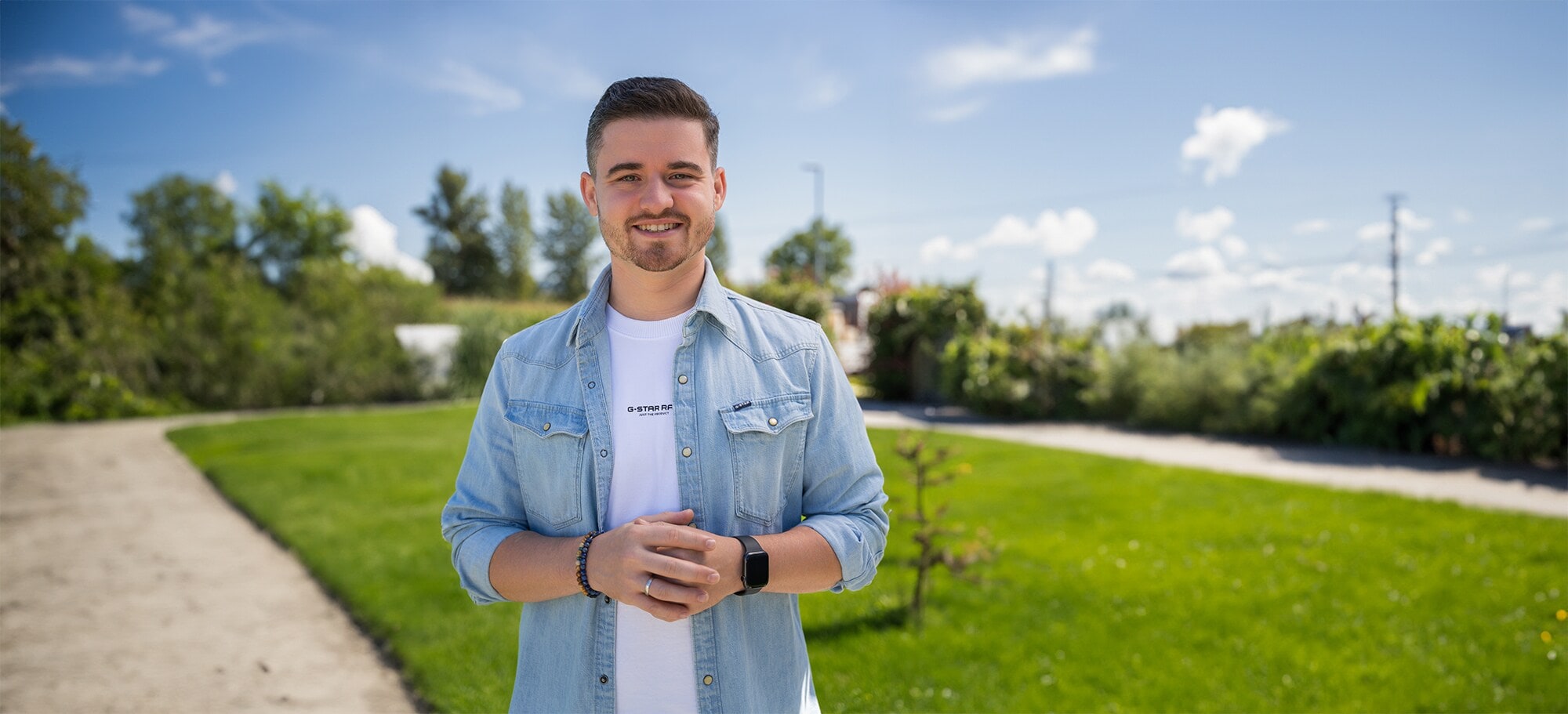 24h Business Platinum: Ein Tag im Leben von Adstark-Gründer Ruslan Ilyassov Adstark-Gründer Ruslan Ilyassov steht in einem Park und lächelt in die Kamera.