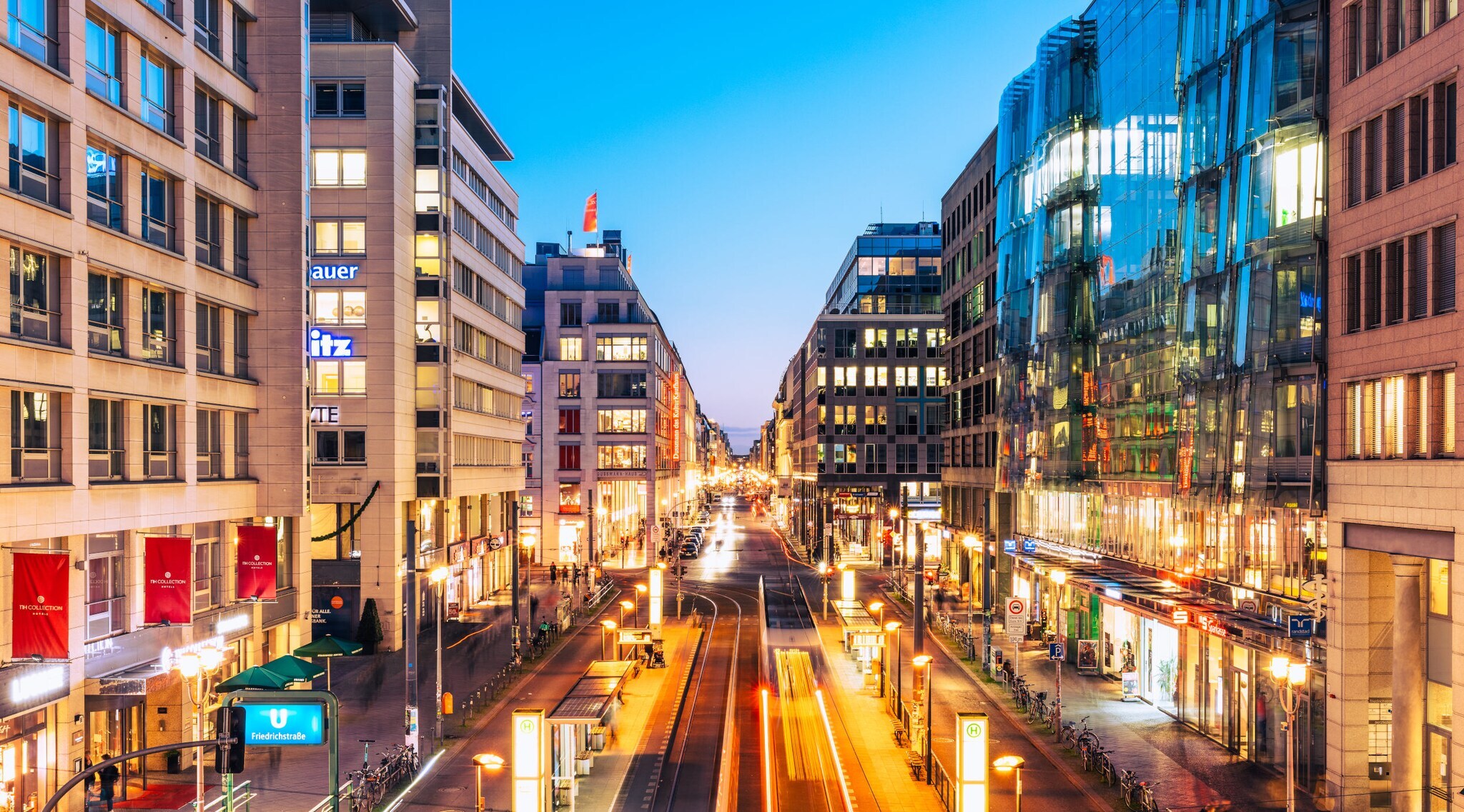 Einkaufsstraße im Stadtzentrum mit beleuchteten Gebäuden bei Abenddämmerung.