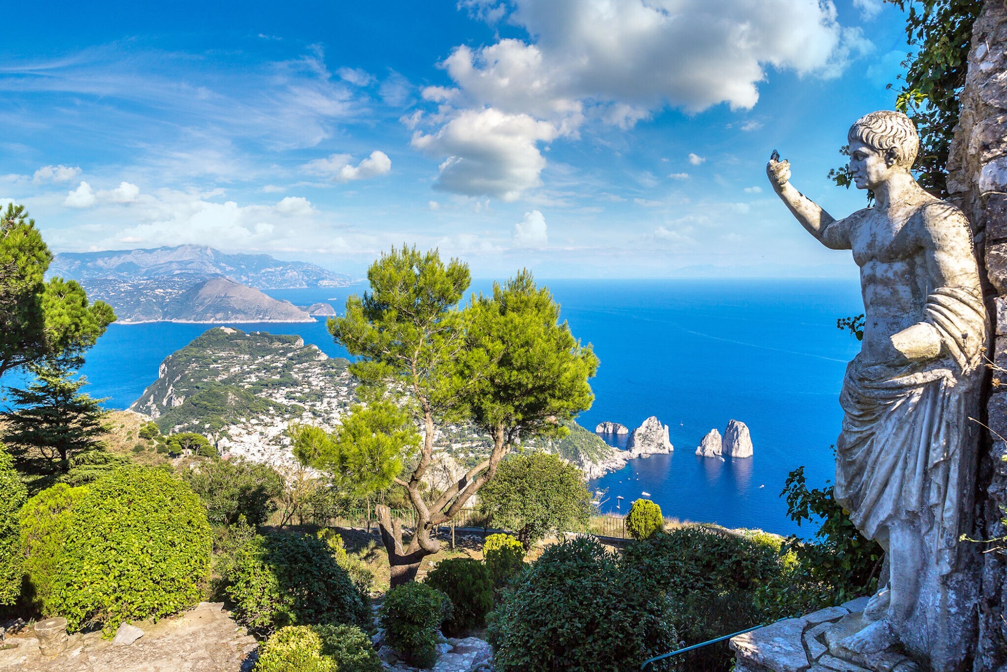 Landschaftspanorama der Insel Capri im blauen Meer, im Vordergrund eine Steinstatue in einem Park.