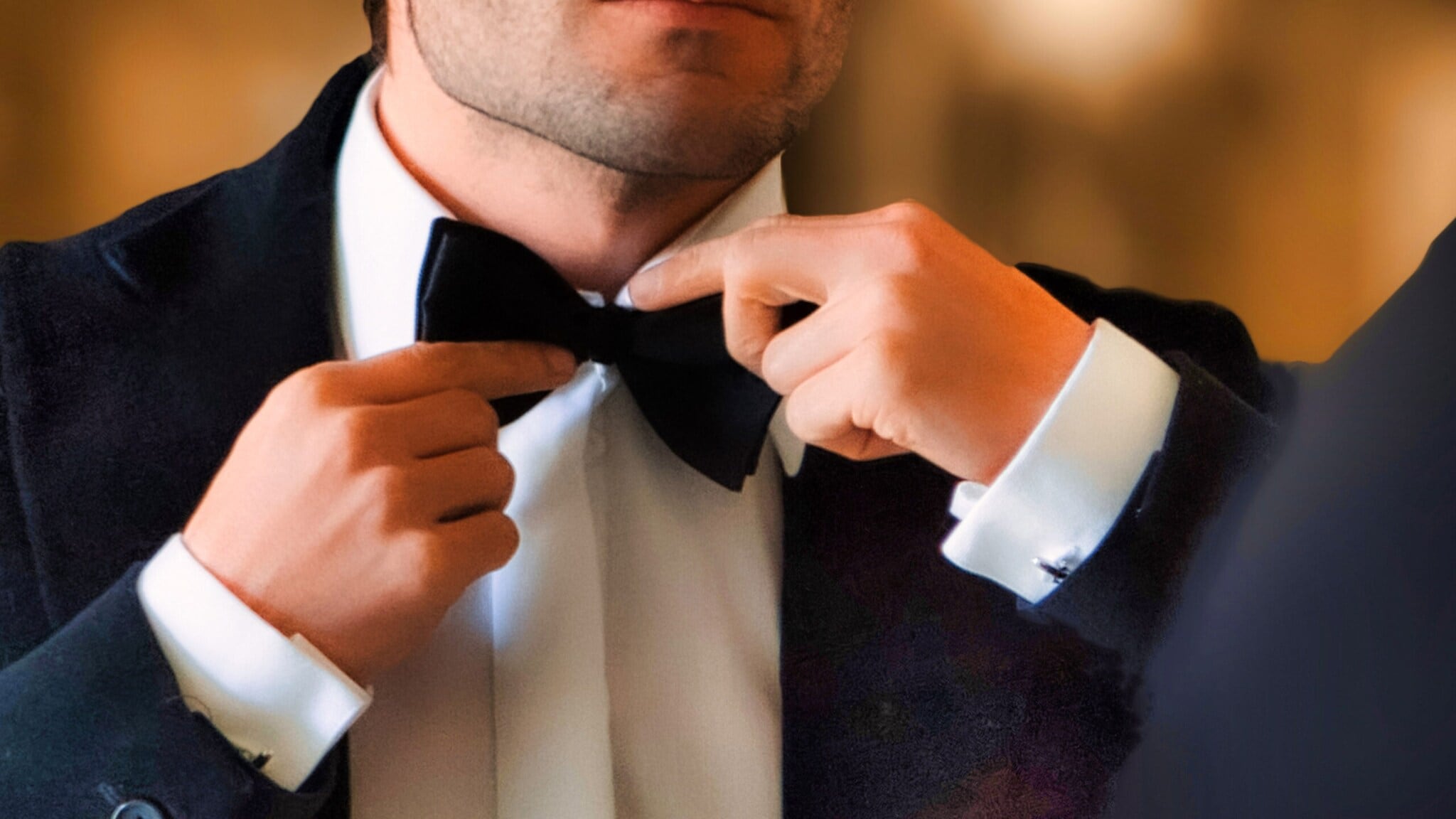 Nahaufnahme von zwei Händen an einer schwarzen Fliege am Hals eines Mannes im Smoking. Nahaufnahme von zwei Händen an einer schwarzen Fliege am Hals eines Mannes im Smoking.