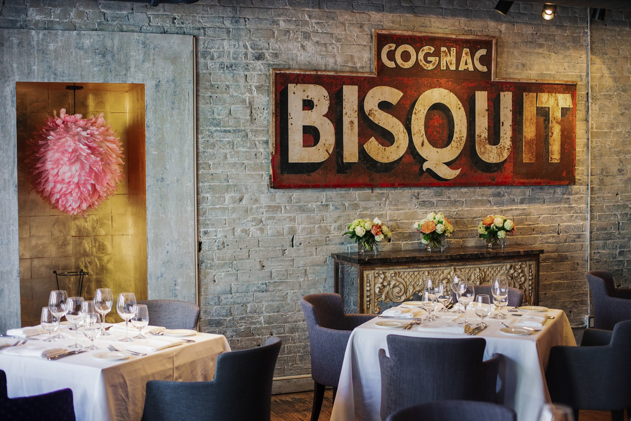 Weiß eingedeckte Restauranttische in einem Raum mit Backsteinwand und antikem Werbeplakat.