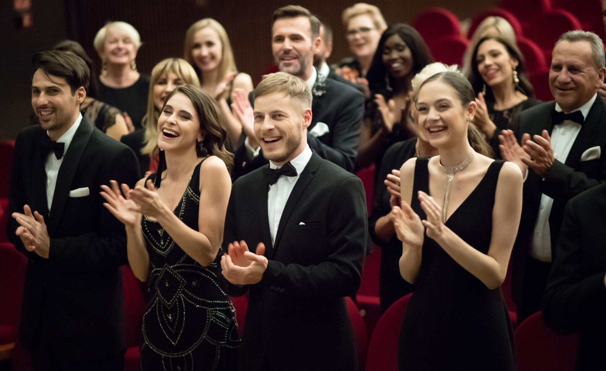Klatschendes Publikum n schwarzer Abendgarderobe in einem Theatersaal vor roten Samtsesseln. Klatschendes Publikum n schwarzer Abendgarderobe in einem Theatersaal vor roten Samtsesseln.