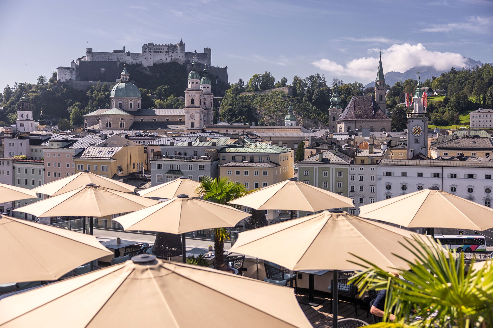 Panorama der Salzburger Altstadt mit Burg auf einem Berg am Fluss, im Hotelterrasse mit Sonnenschirmen.