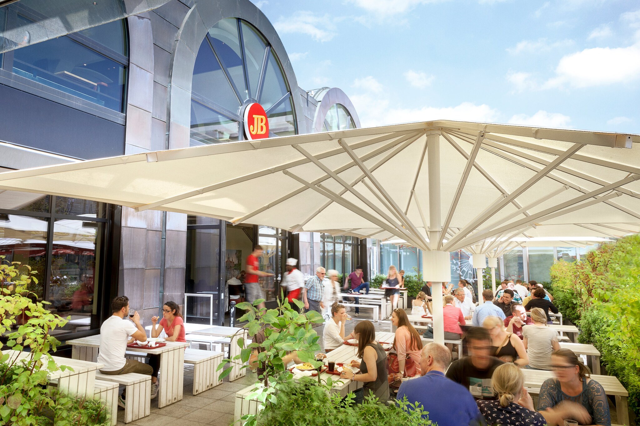 Außengastronomie auf einer Terrasse an einer Jim Block Filiale mit moderner Glasfassade.