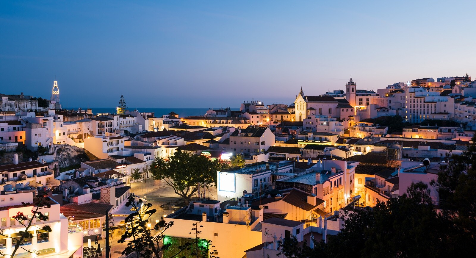 Blick auf die Skyline von Albufeira mit ihren weißen, beleuchteten Häusern bei Nacht.