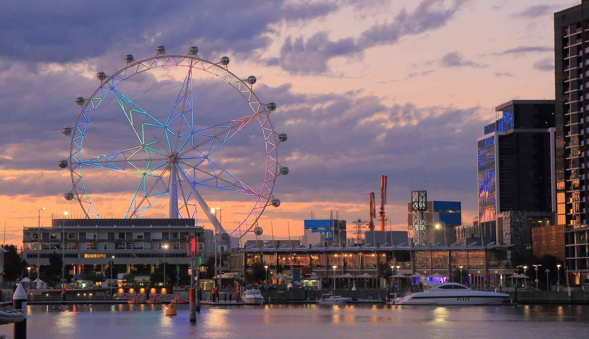 Stadtpanorama mit erleuchtetem Riesenrad an einer Waterfront bei Abenddämmerung.