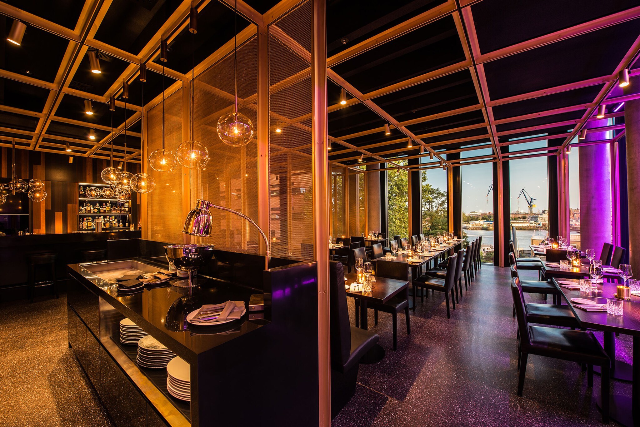 Offener Speiseraum eines stylishen Restaurants mit Blick auf Hafenareal durch Panoramafenster.