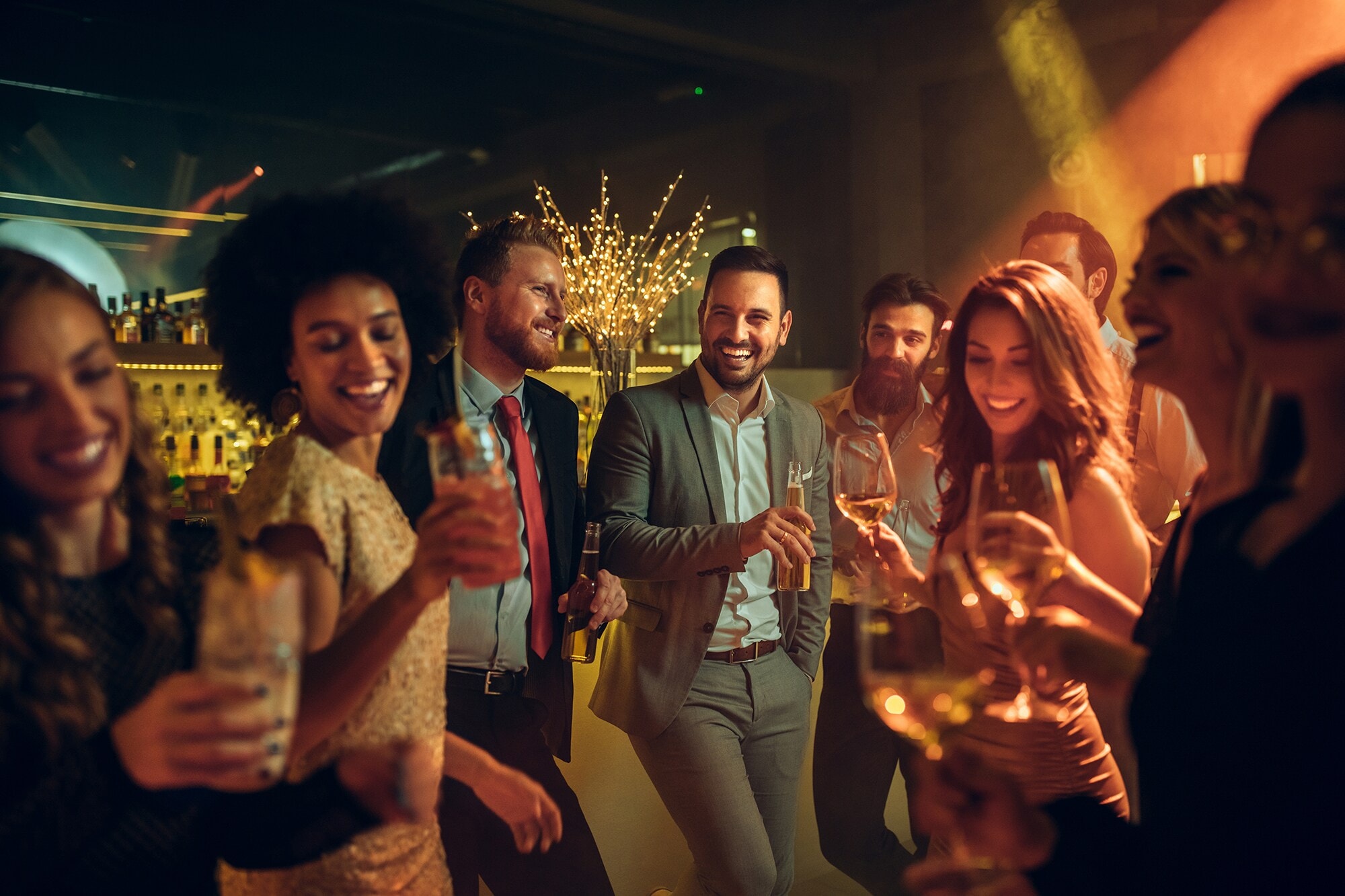 Let’s Party: Business-Dresscodes und Style-Tipps für festliche Zeiten Eine Gruppe elegant gekleideter Frauen und Männer feiert in einem Club.