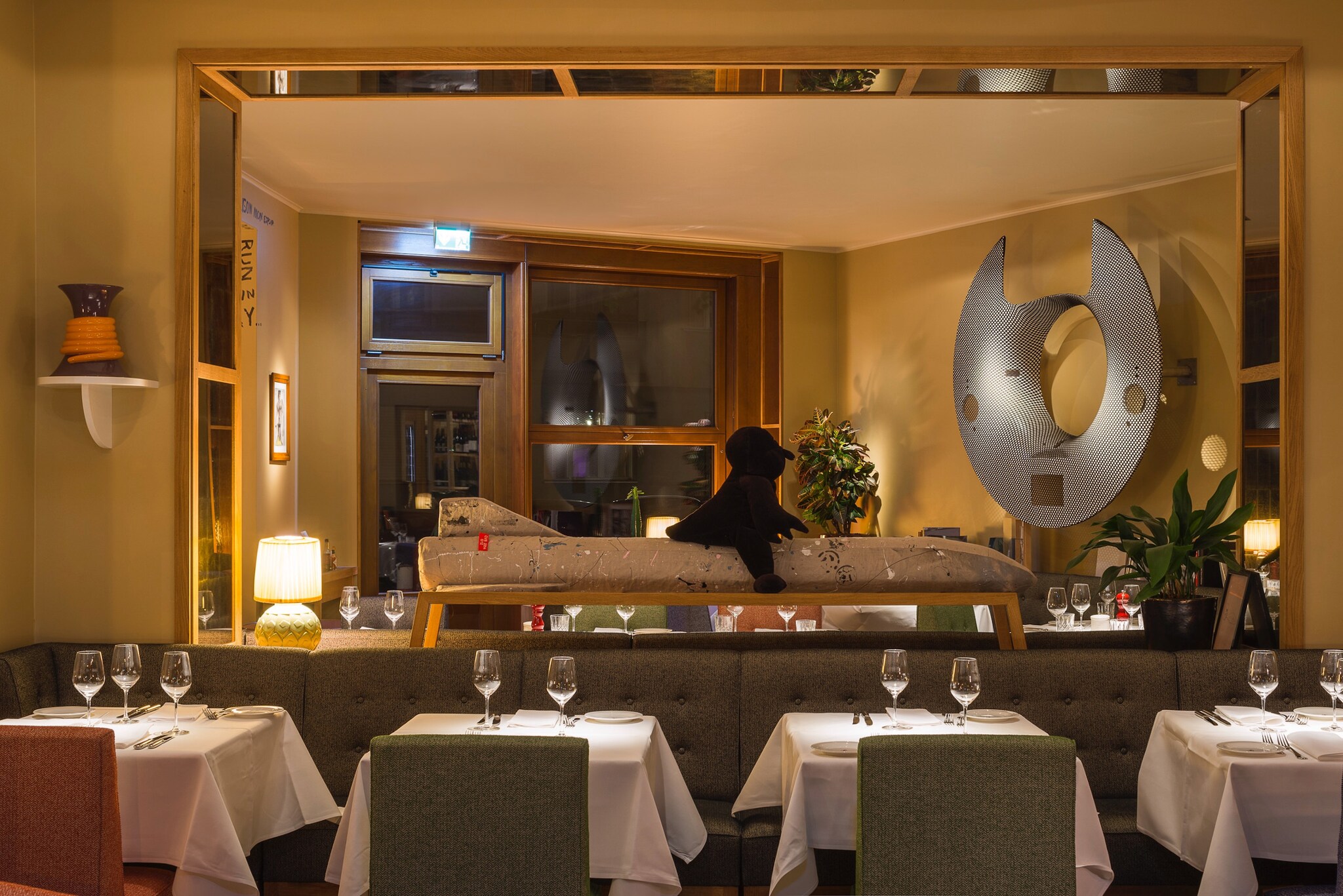 Stilvolles Restaurant mit Kunstobjekten und eingedeckten Tischen an Polsterbank.