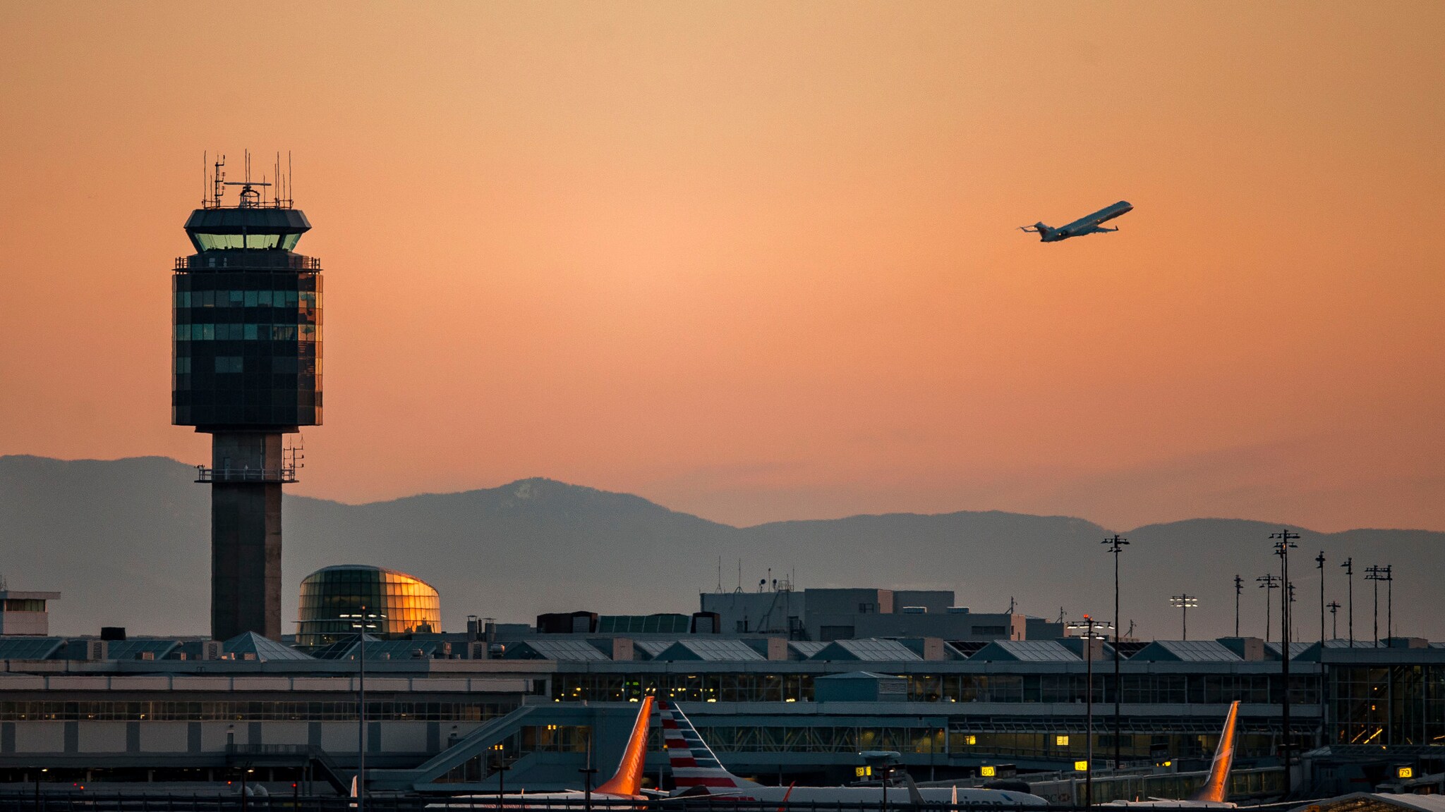 Tower des Vancouver Airports bei Sonnenuntergang und ein startendes Flugzeug.