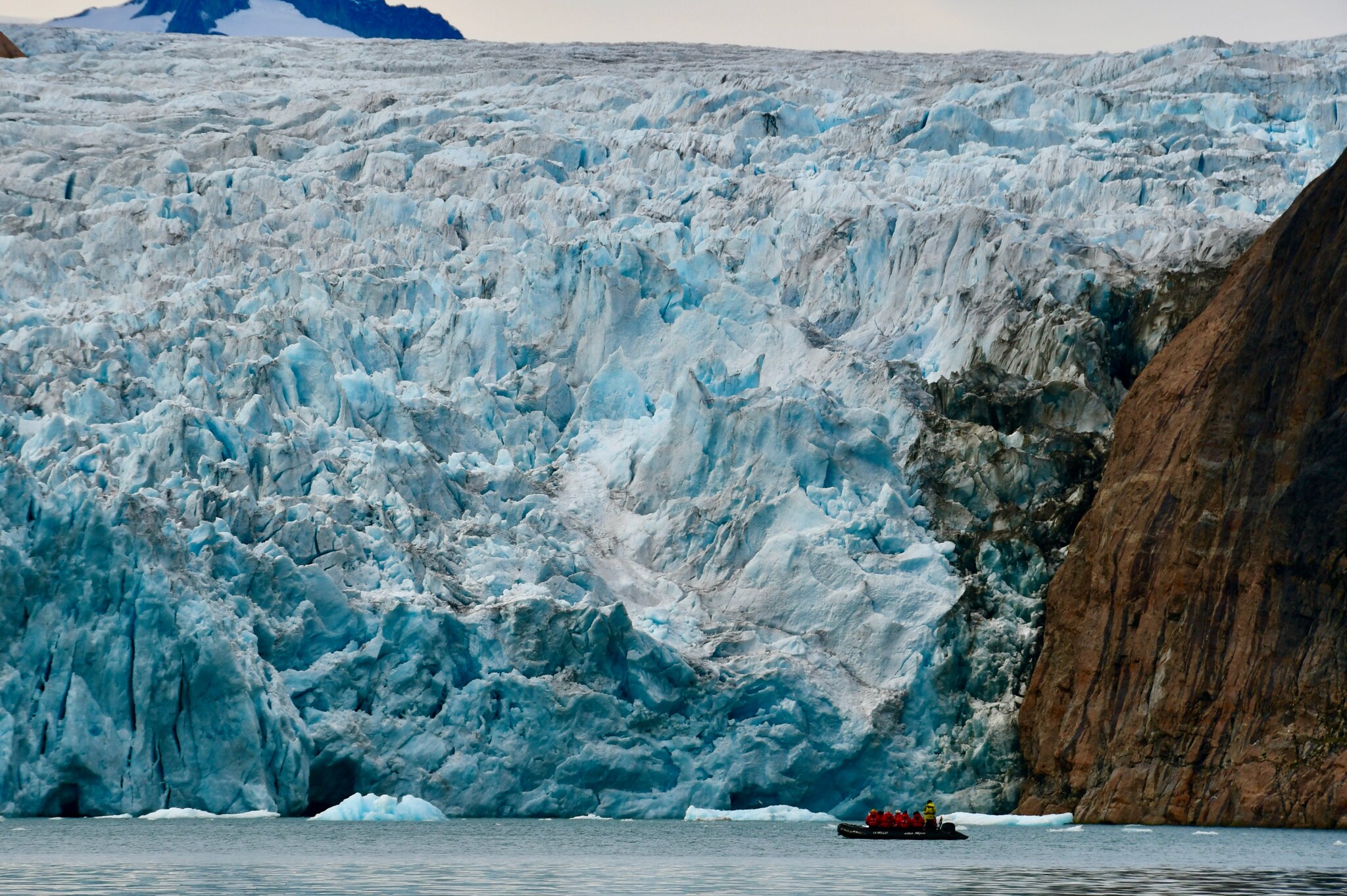 Das Bild zeigt einen riesigen Gletscher, der in das Wasser des Meeres mündet. Im Vordergrund ist ein Schlauchboot mit Gästen der Kreuzfahrt zu sehen.