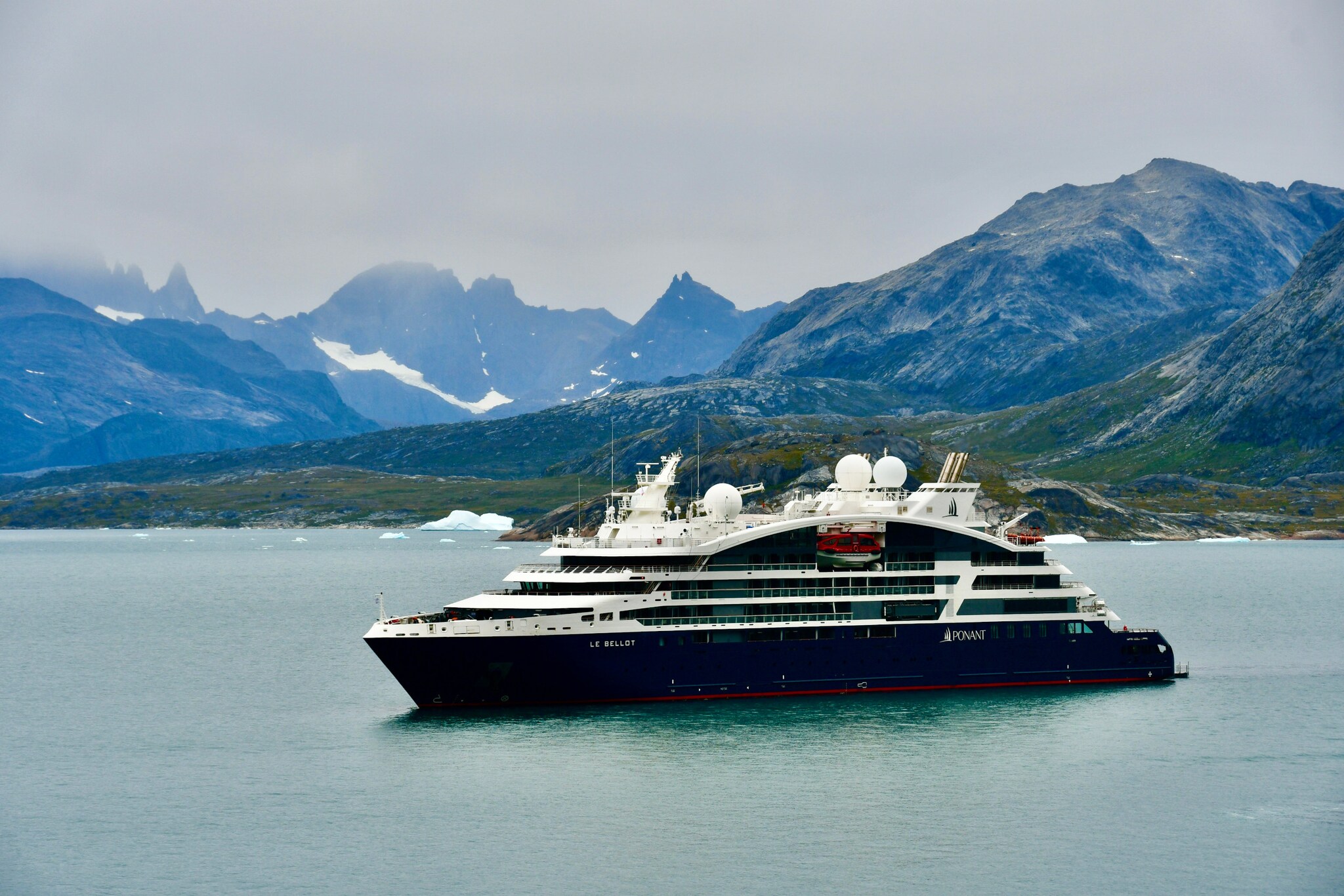 Das Bild zeigt im Vordergrund das Kreuzfahrtschiff. Im Hintergrund sind Berge und etwas Schnee und Eis zu sehen.