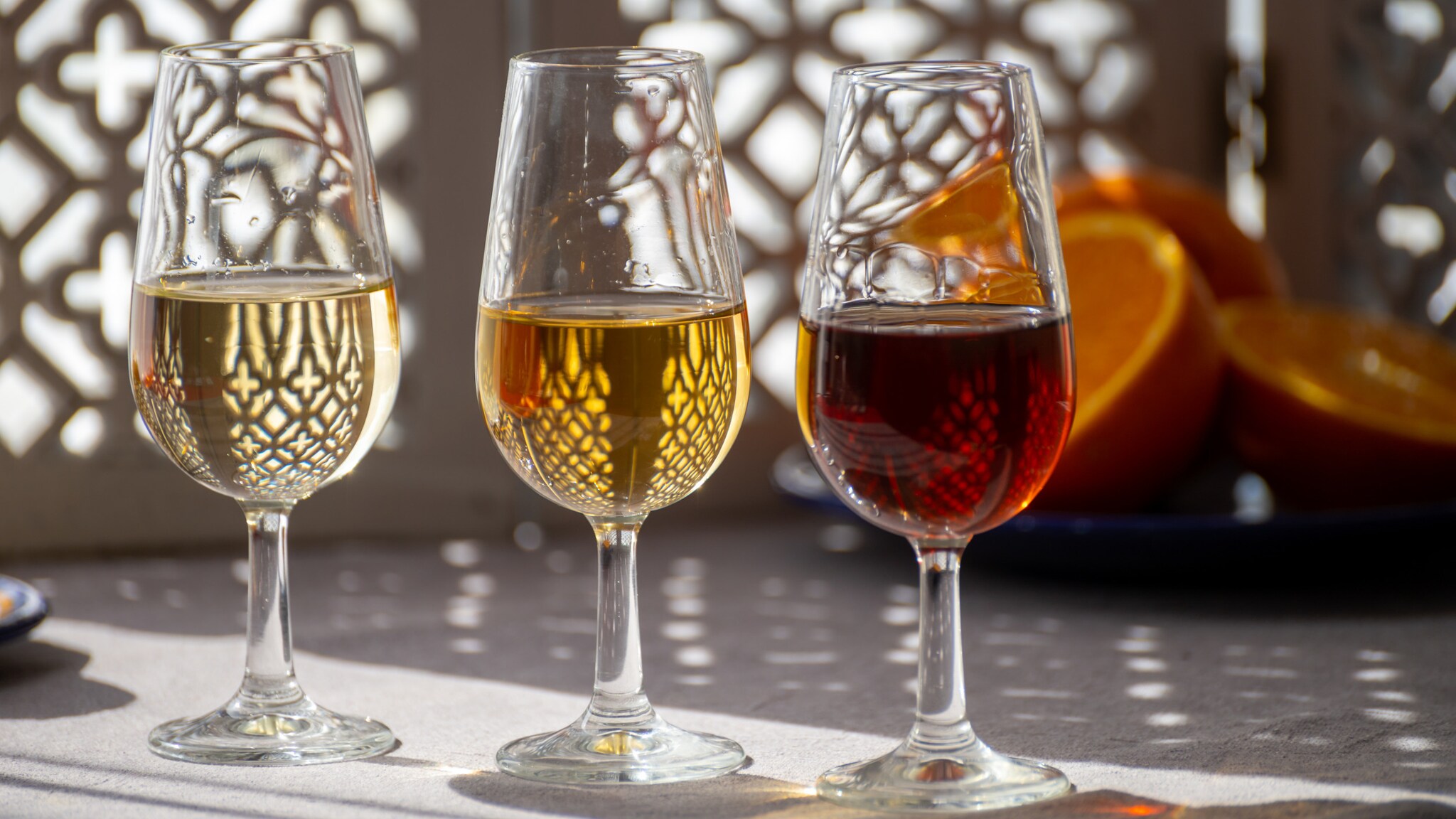 Drei Gläser gefüllt mit Sherry in verschiedenen Farben, im Hintergrund liegen Orangenhälften. Drei Gläser gefüllt mit Sherry in verschiedenen Farben, im Hintergrund liegen Orangenhälften.