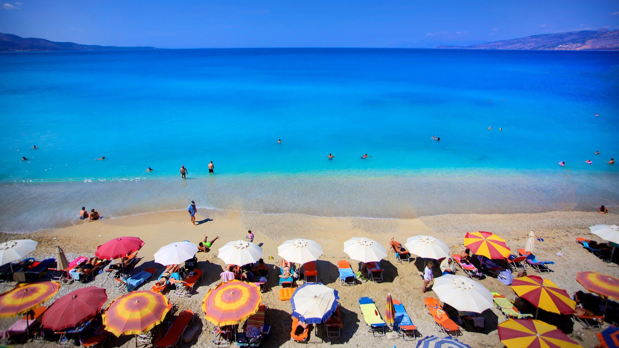 Aufsicht eines Sandstrandes mit Liegen und Sonnenschirmen am Meer mit Wasser von starker blauer Farbintensivität. Aufsicht eines Sandstrandes mit Liegen und Sonnenschirmen am Meer mit Wasser von starker blauer Farbintensivität.