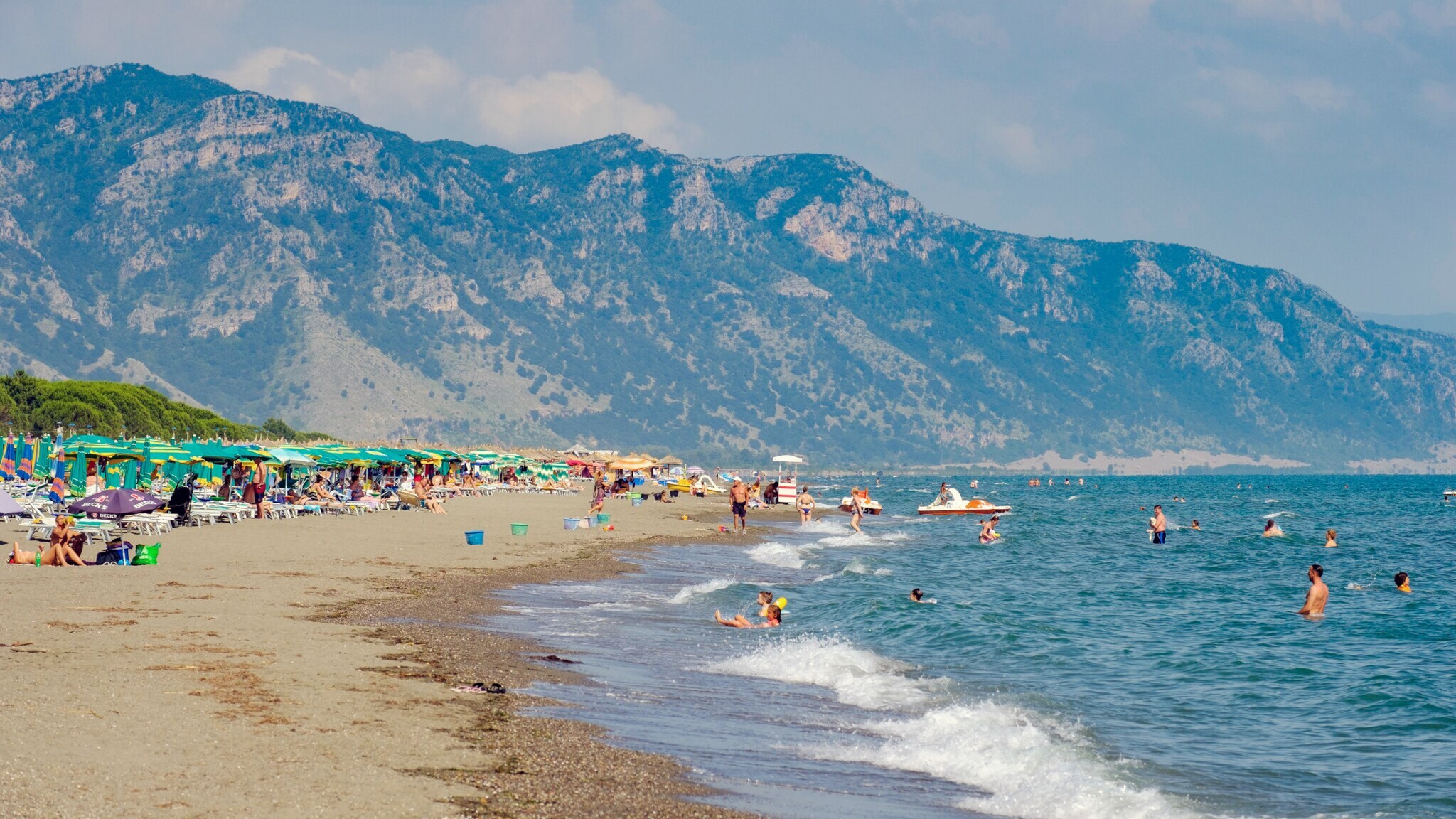 Sandstrand mit Personen in und am Wasser vor Bergpanorama. Sandstrand mit Personen in und am Wasser vor Bergpanorama.