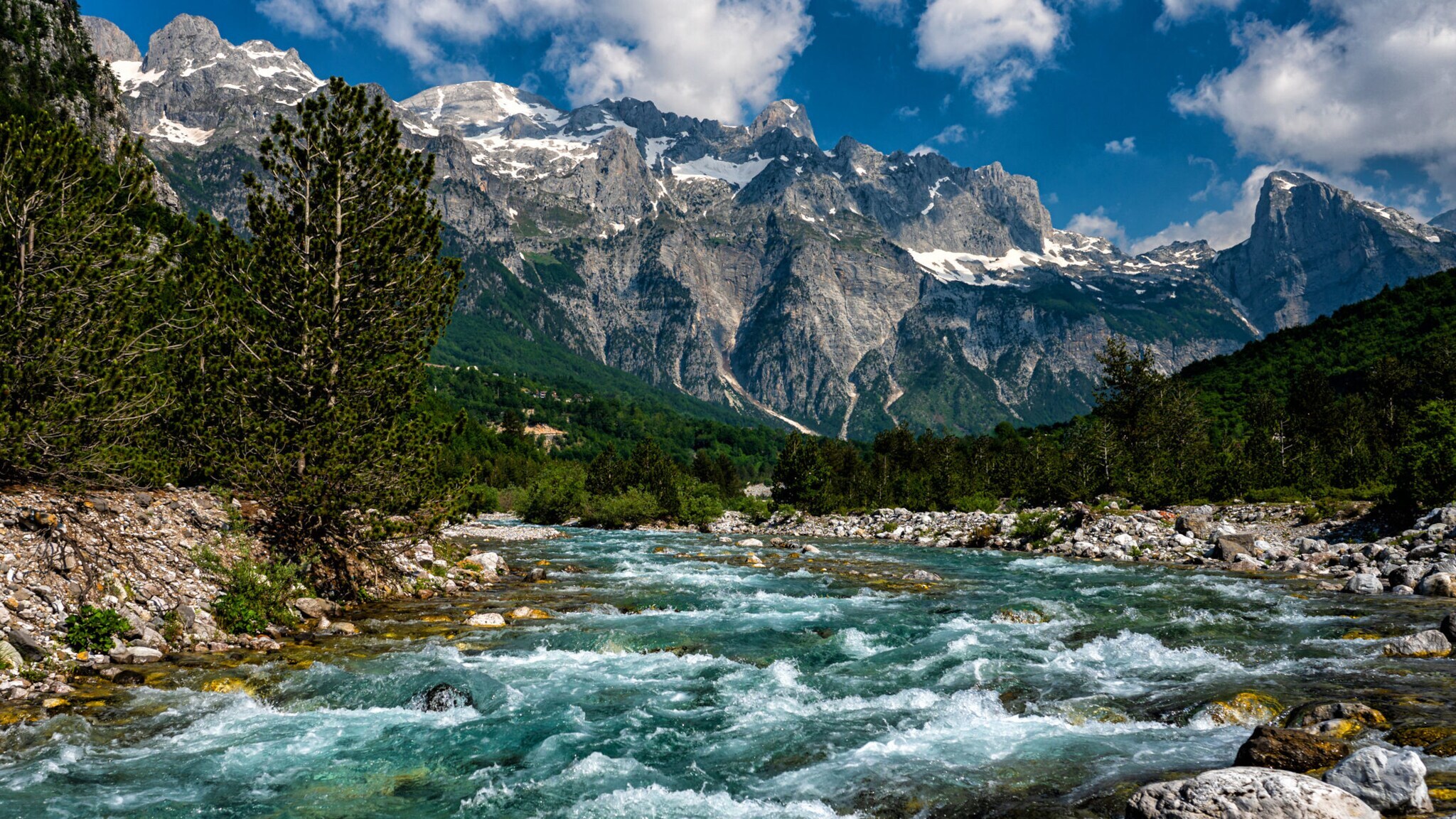 Fluss im Nationalpark Theth in Albanien mit schneebedeckten Gipfel im Hintergrund.