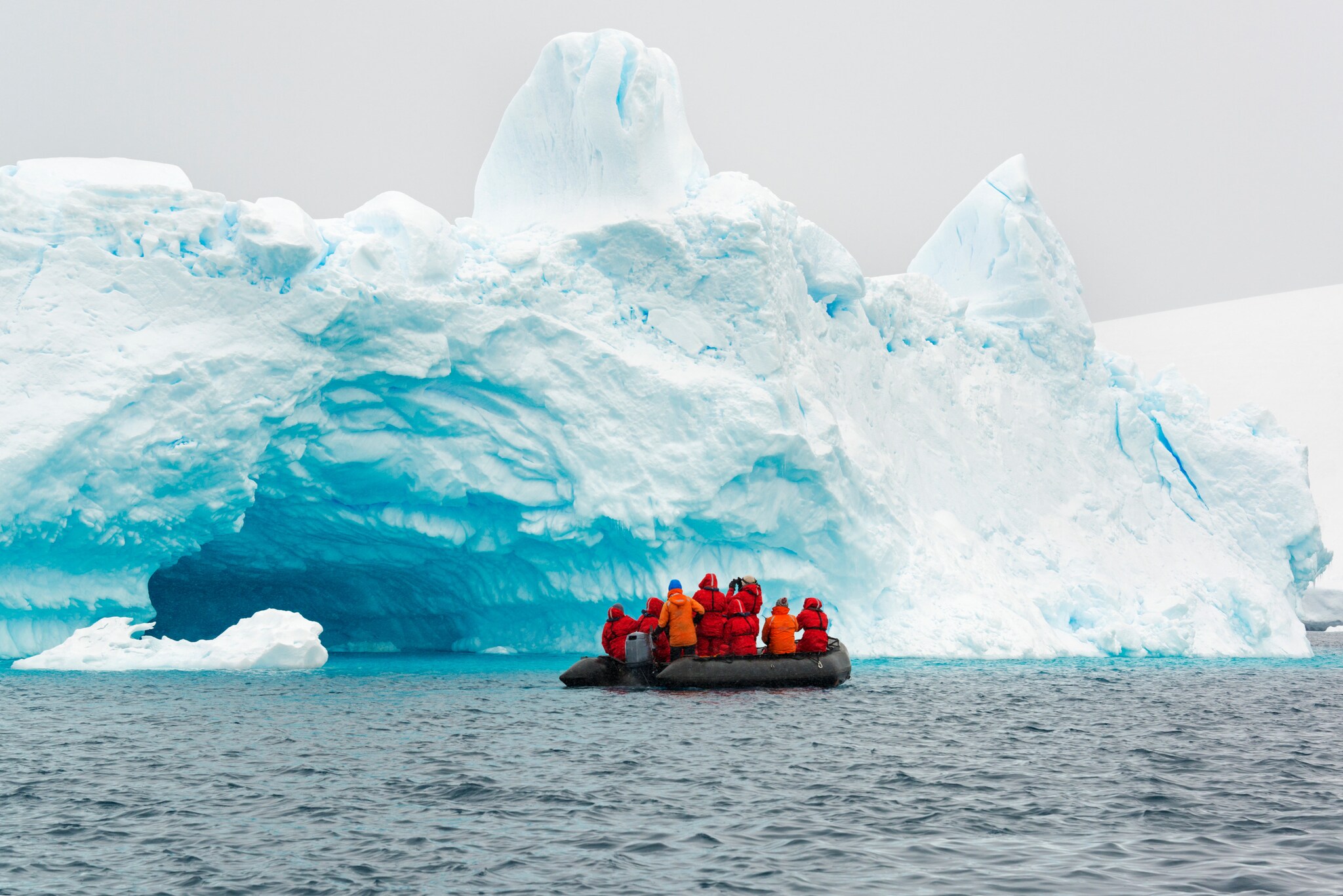 Personen auf einem Schlauchboot vor einer Eiswand im Wasser.