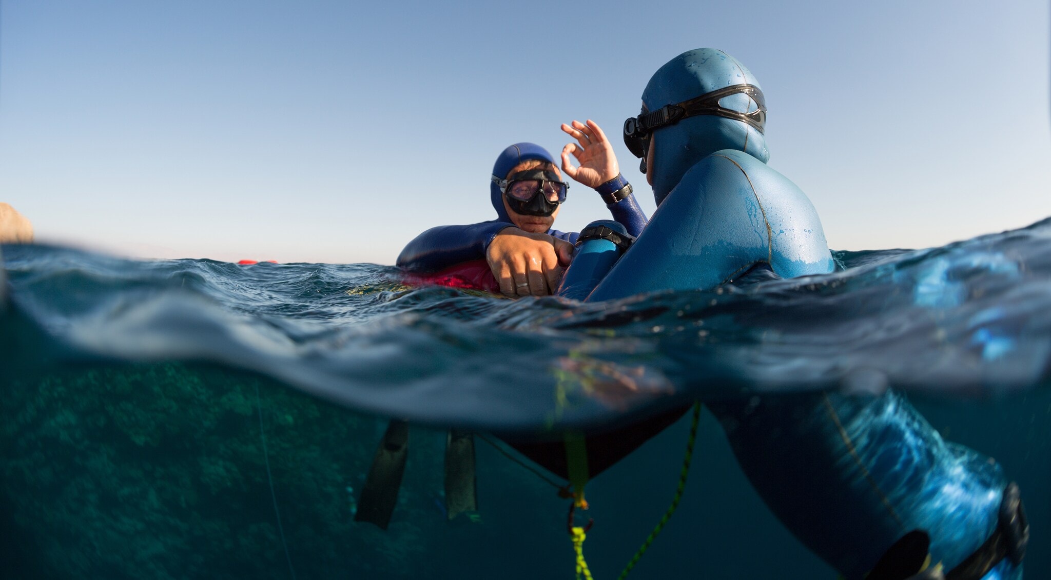 Zwei Freitaucher in Neoprenanzügen kommunizieren durch Handzeichen an einer Boje im Wasser. Zwei Freitaucher in Neoprenanzügen kommunizieren durch Handzeichen an einer Boje im Wasser.