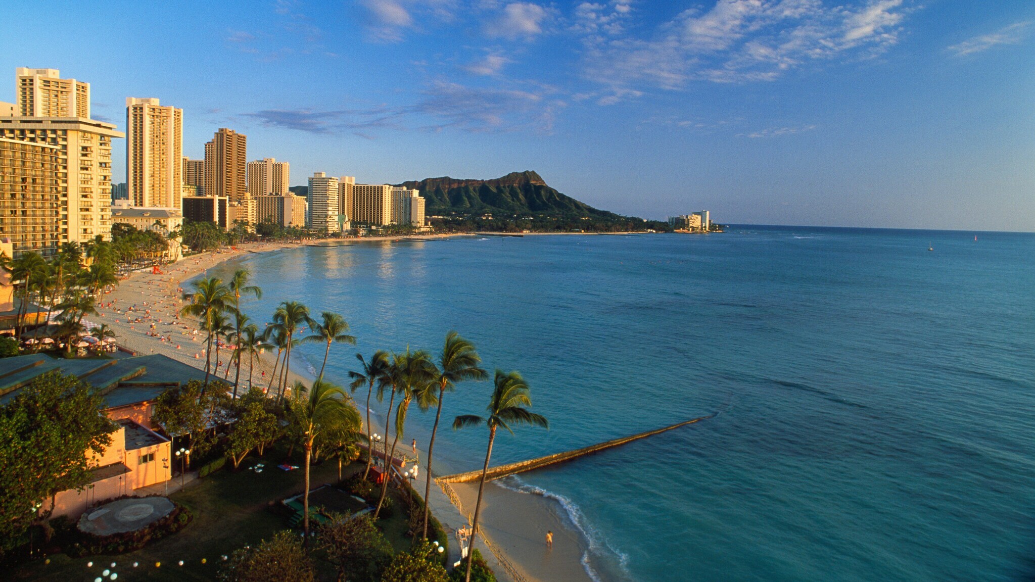Skyline in einer weitläufigen Bucht mit Palmen und Sandstrand in goldenem Sonnenlicht.
