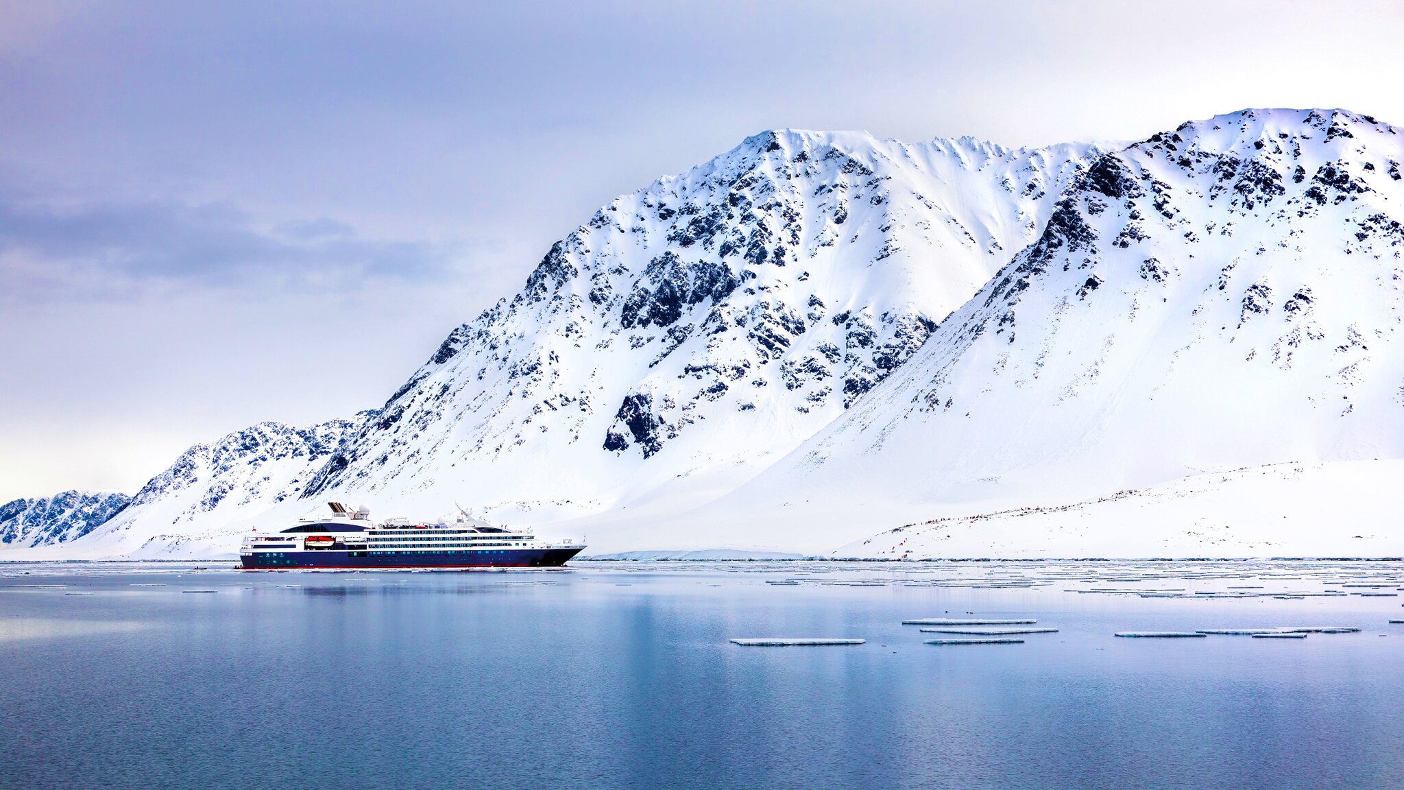 Ein Expeditionsschiff im arktischen Gewässer vor schneebedeckten Bergen. Ein Expeditionsschiff im arktischen Gewässer vor schneebedeckten Bergen.