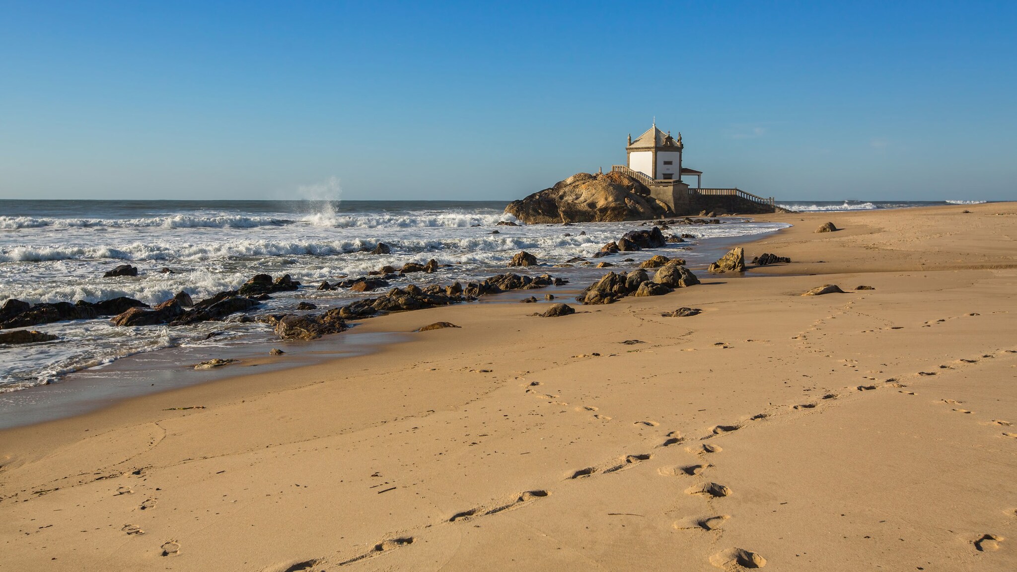Praia da Miramar in Portugal mit Felsen, auf dem eine kleine Kapelle steht.