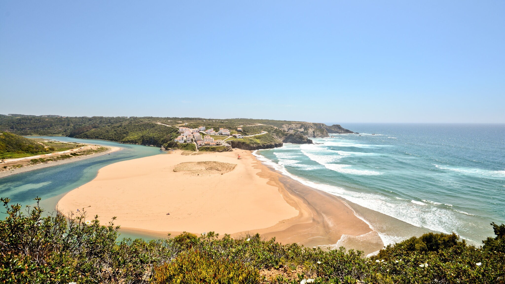 Luftaufnahme der Praia de Odeceixe mit Fluss auf der einen und Meer auf der anderen Seite.