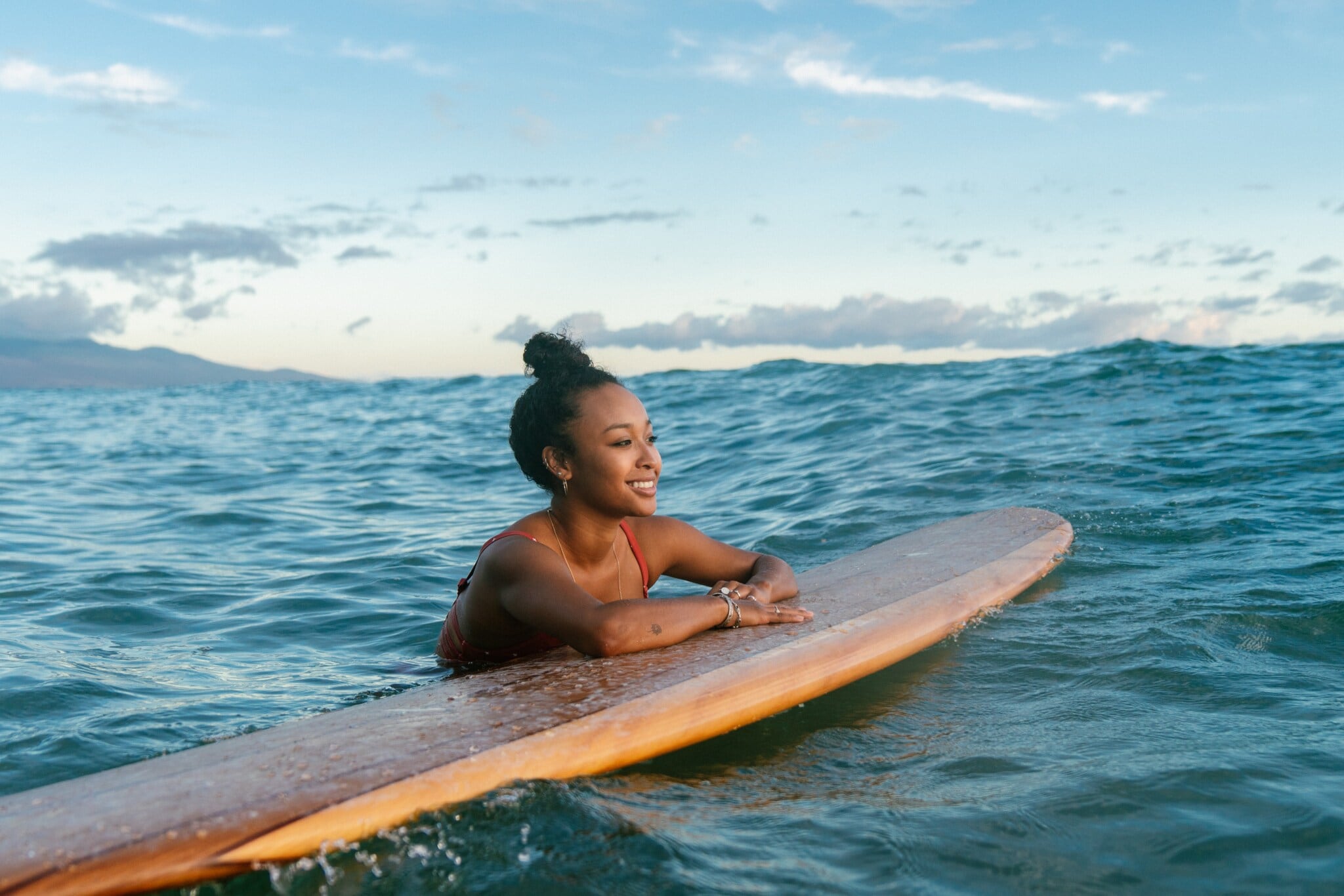 Eine lächelnde Frau hängt lässig mit den Armen an einem Surfbrett im Meer. Eine lächelnde Frau hängt lässig mit den Armen an einem Surfbrett im Meer.