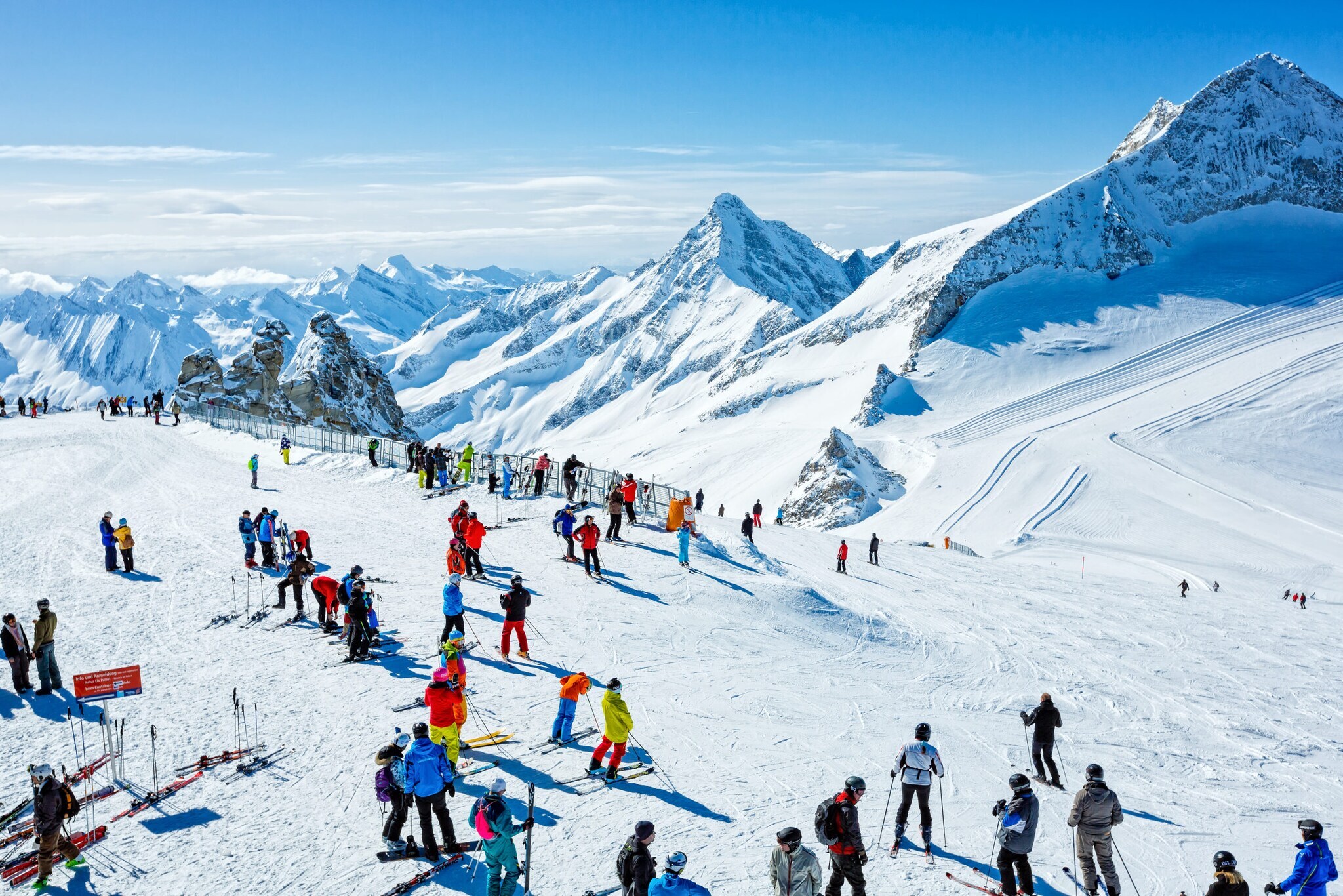 Skifahrende auf einem Plateau auf einer Skipiste vor schneebedecktem Gipfelpanorama.