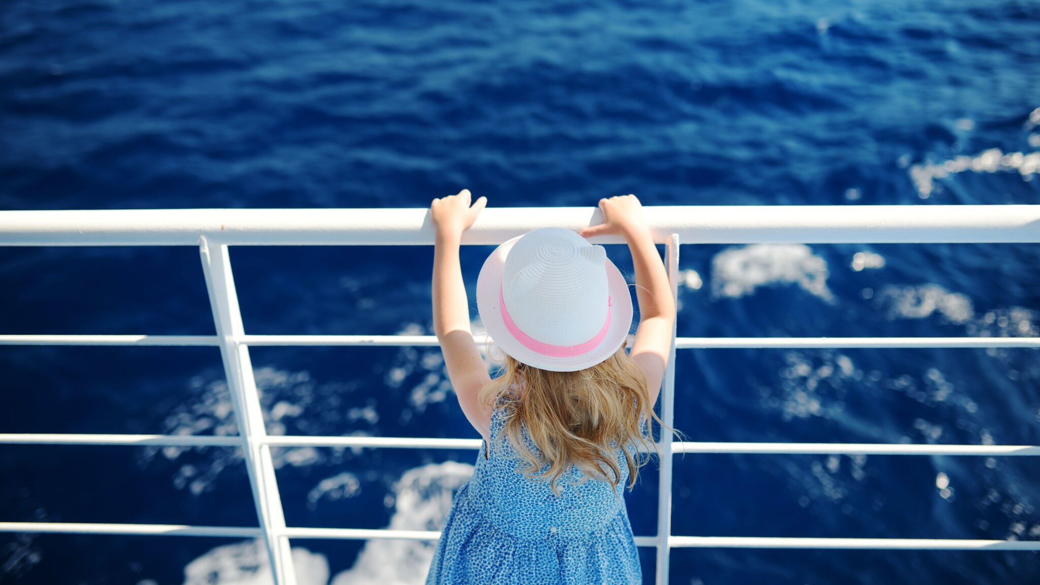 Rückansicht eines Mädchens mit weißem Hut an der Reling eines Schiffes auf dem Meer.
