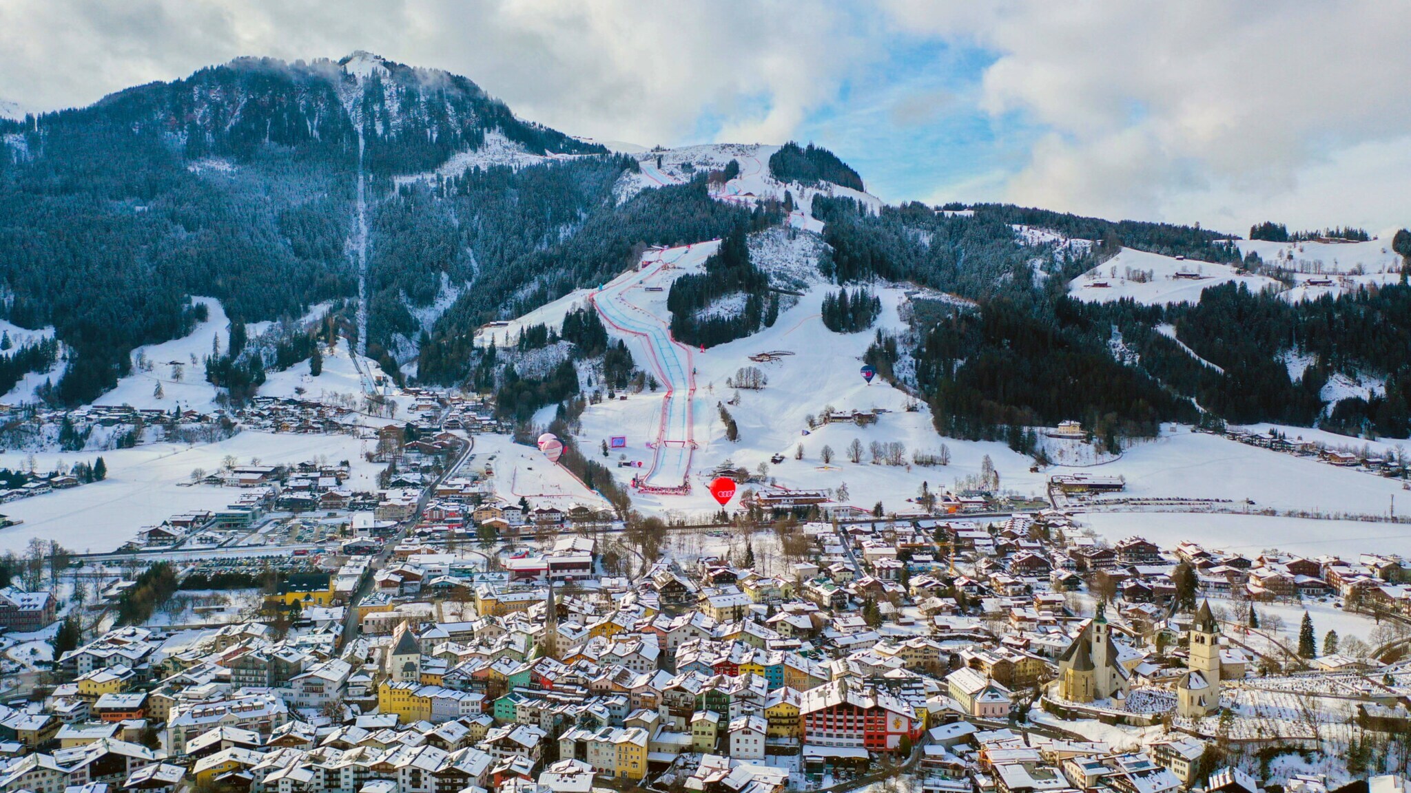 Schneebedecktes Stadtpanorama von Kitzbühel vor Berg mit Skipisten.