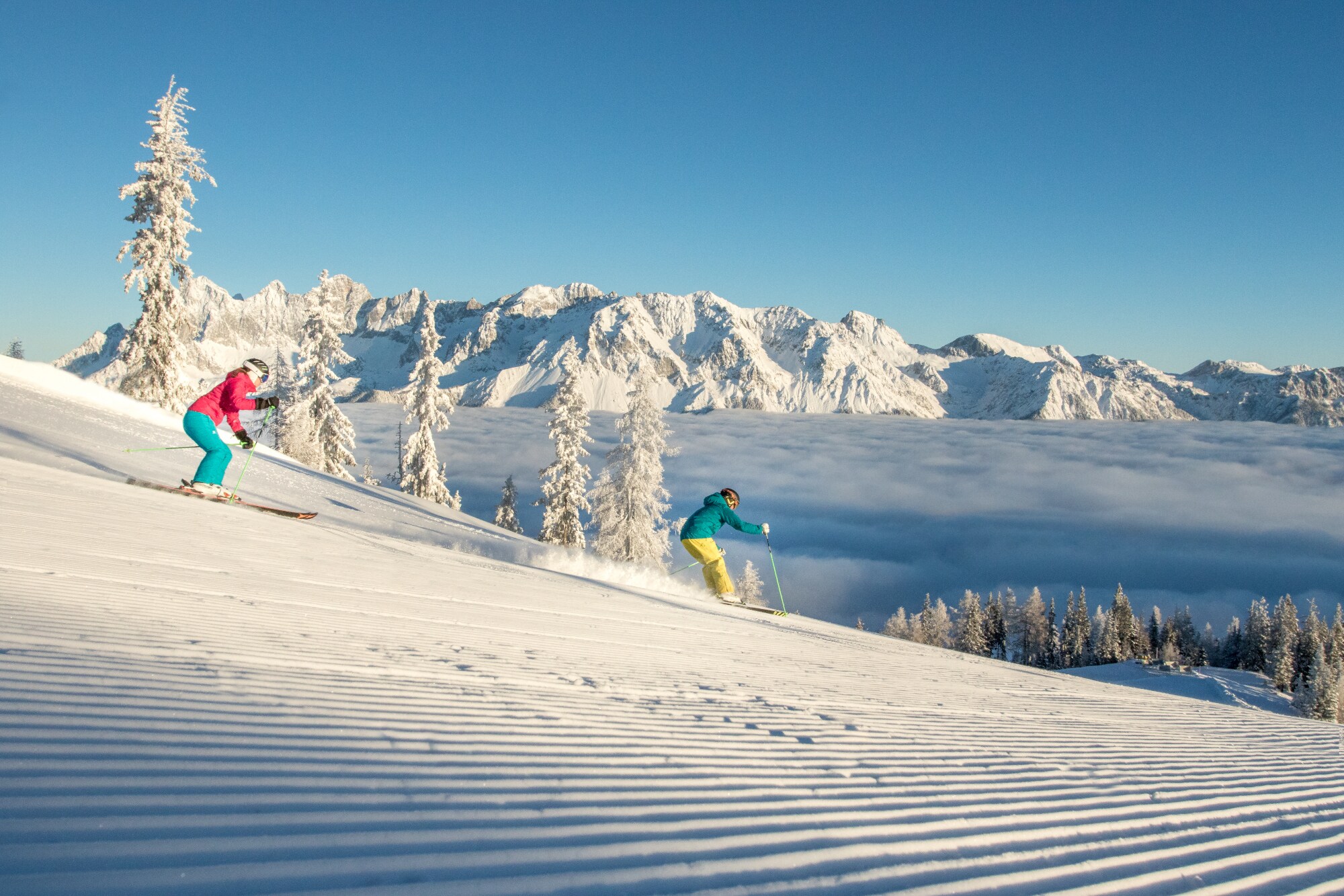 Zwei Skifahrende auf einer Piste bei der Abfahrt oberhalb der Wolkendecke vor schneebedeckten Gipfeln. Zwei Skifahrende auf einer Piste bei der Abfahrt oberhalb der Wolkendecke vor schneebedeckten Gipfeln.