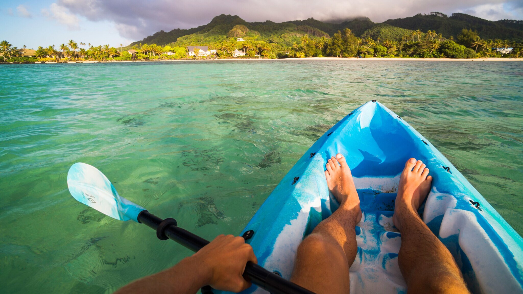 Nackte Beine on einem blauen Kanu auf dem Wasser vor tropischer Küstenlandschaft.