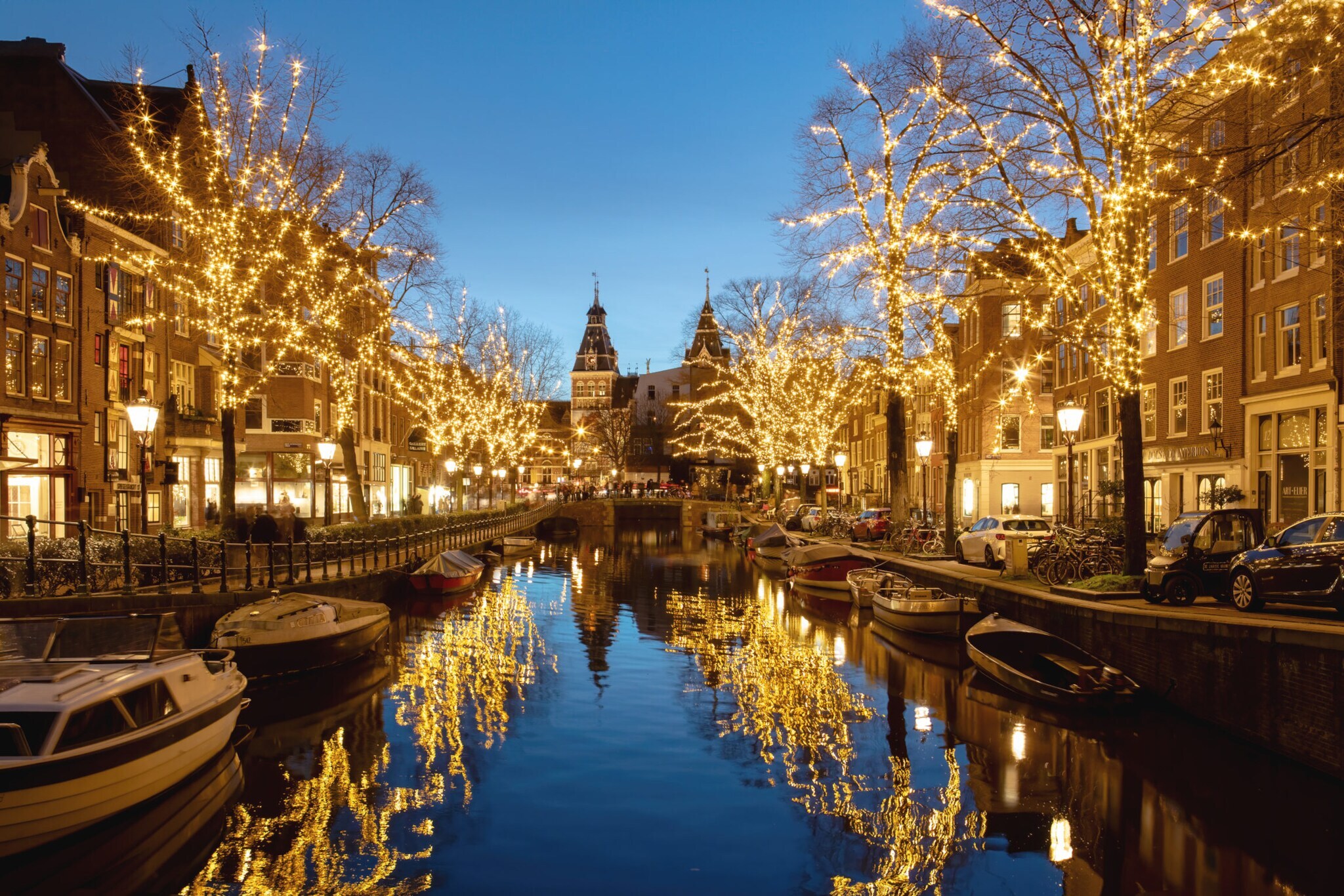 Gracht mit von Lichterketten beleuchteten Bäumen am Abend.