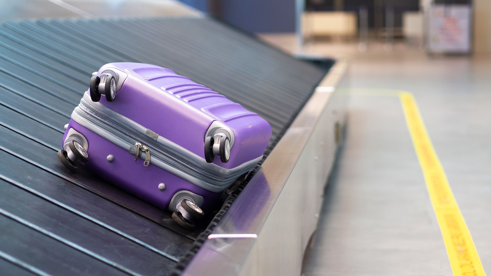 Ein einzelner, lilafarbener Hartschalenkoffer auf einem Gepäckband am Flughafen. Ein einzelner, lilafarbener Hartschalenkoffer auf einem Gepäckband am Flughafen.