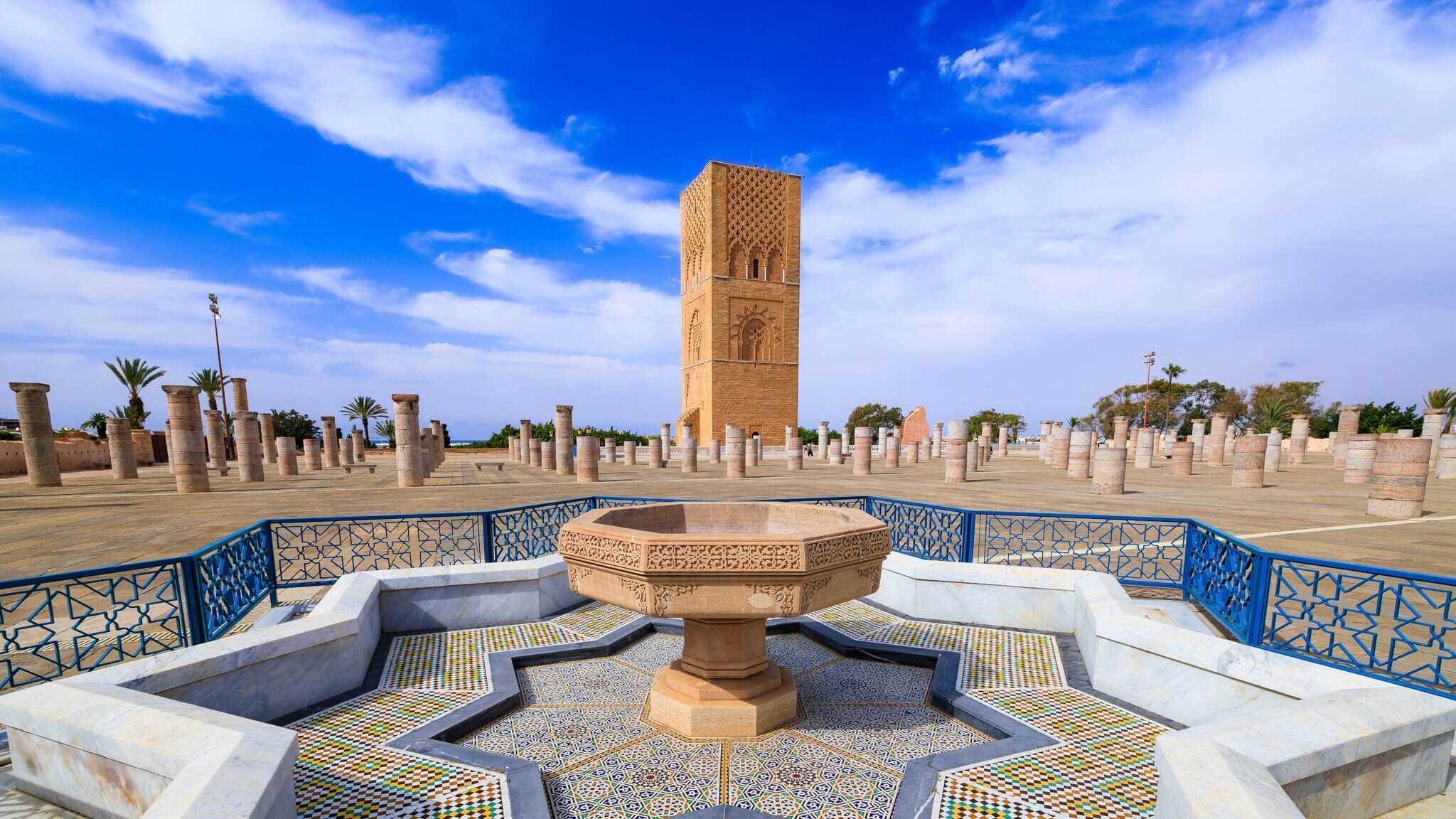 Halbfertiges Minarett im maurischen Stil auf einem Platz mit sternförmigem, stillgelegtem Brunnen im Vordergrund.