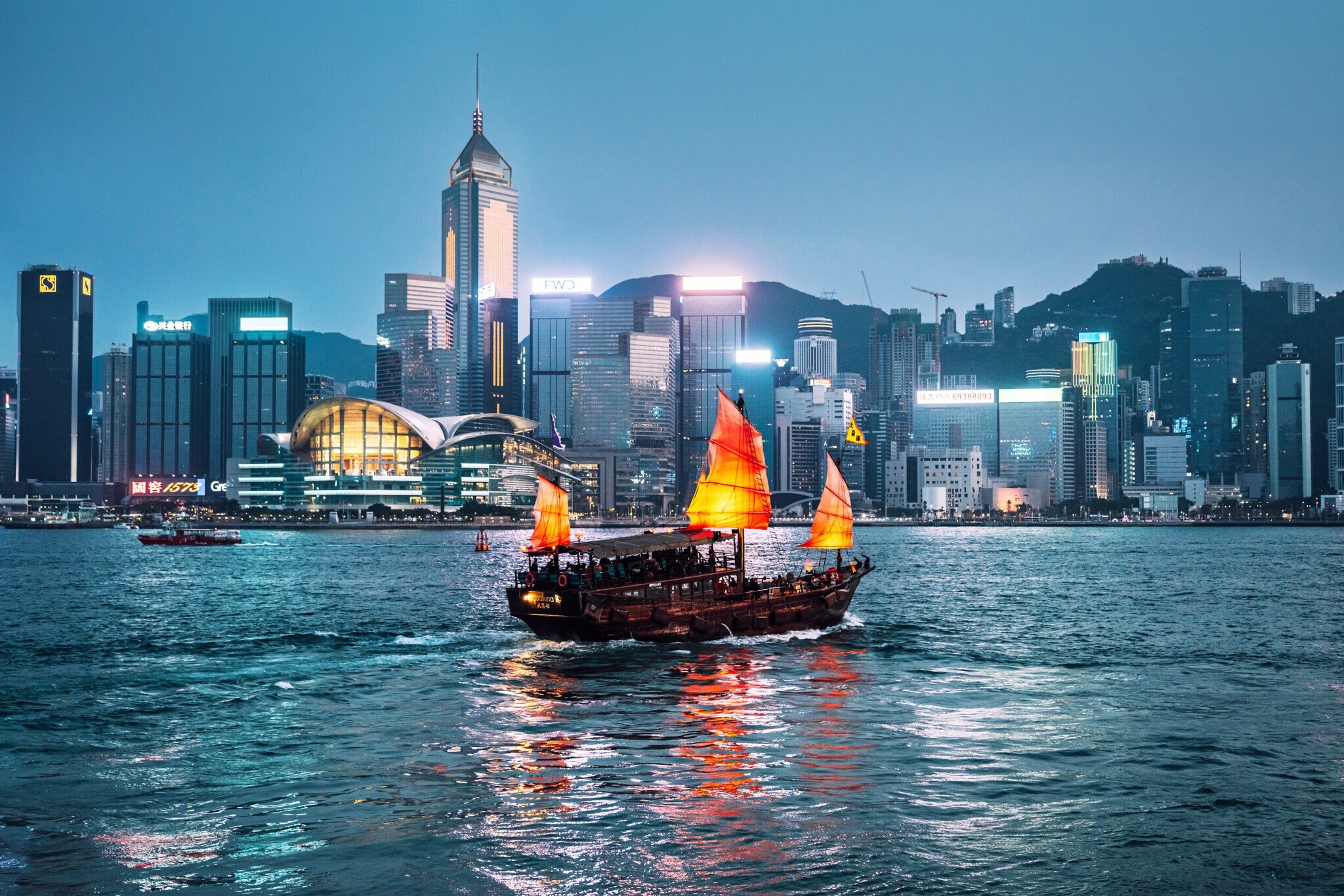 Rote chinesische Dschunke auf dem Wasser vor der Skyline Hongkongs bei Nacht.