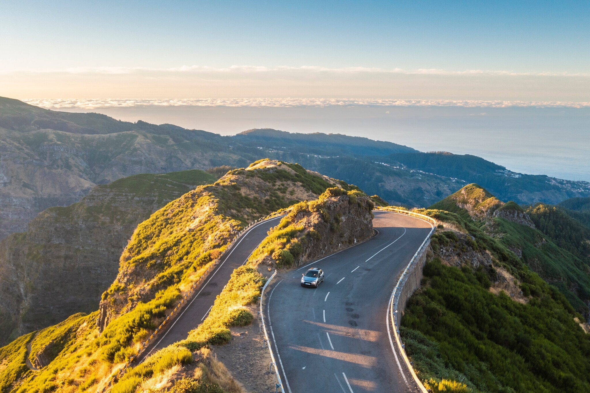 Ein Auto auf einer kurvigen Straße durch eine hügelige Landschaft auf Madeira.