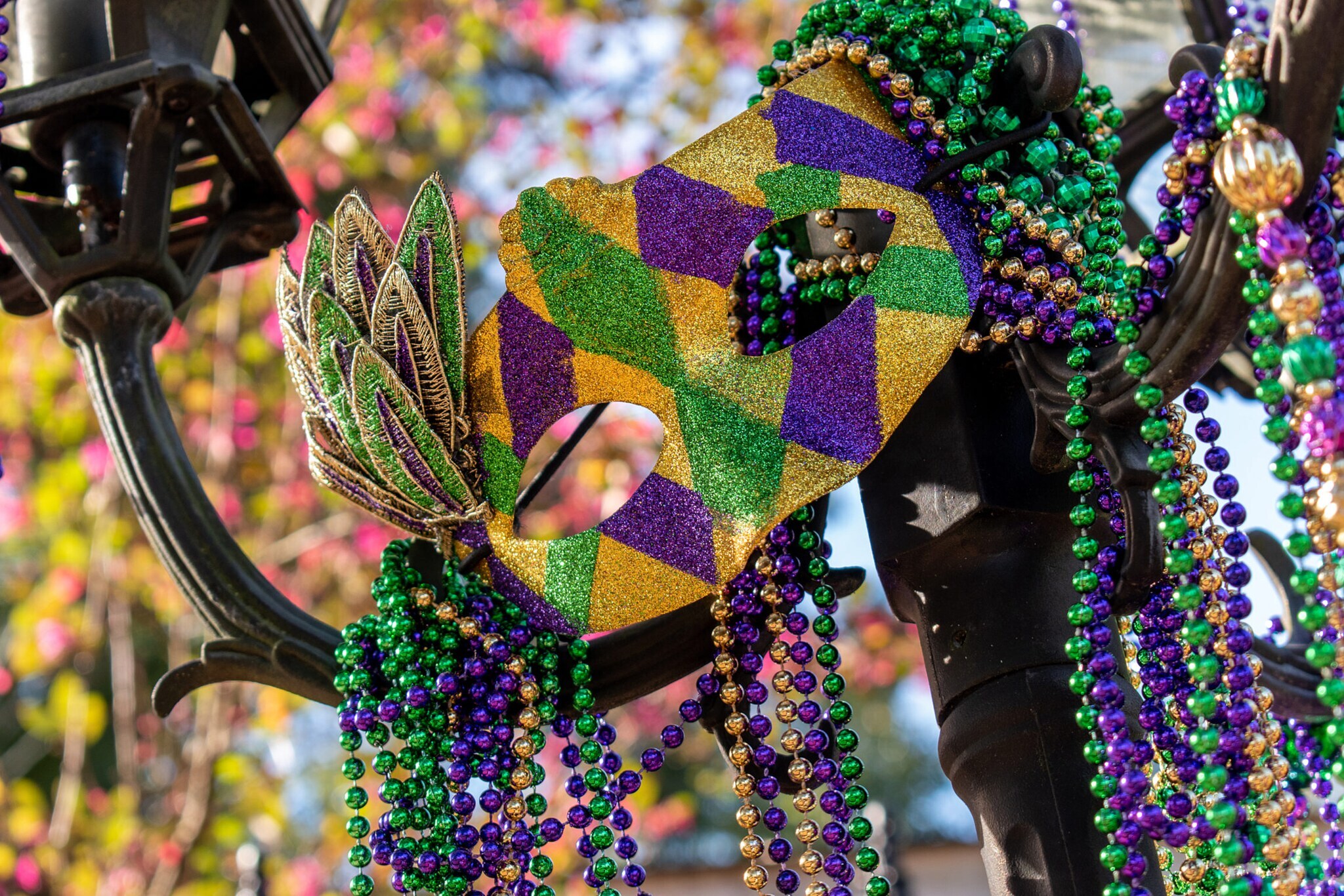 Eine Maske und Perlenketten in den Farben Grün, Gold und Violett an einer Straßenlaterne.