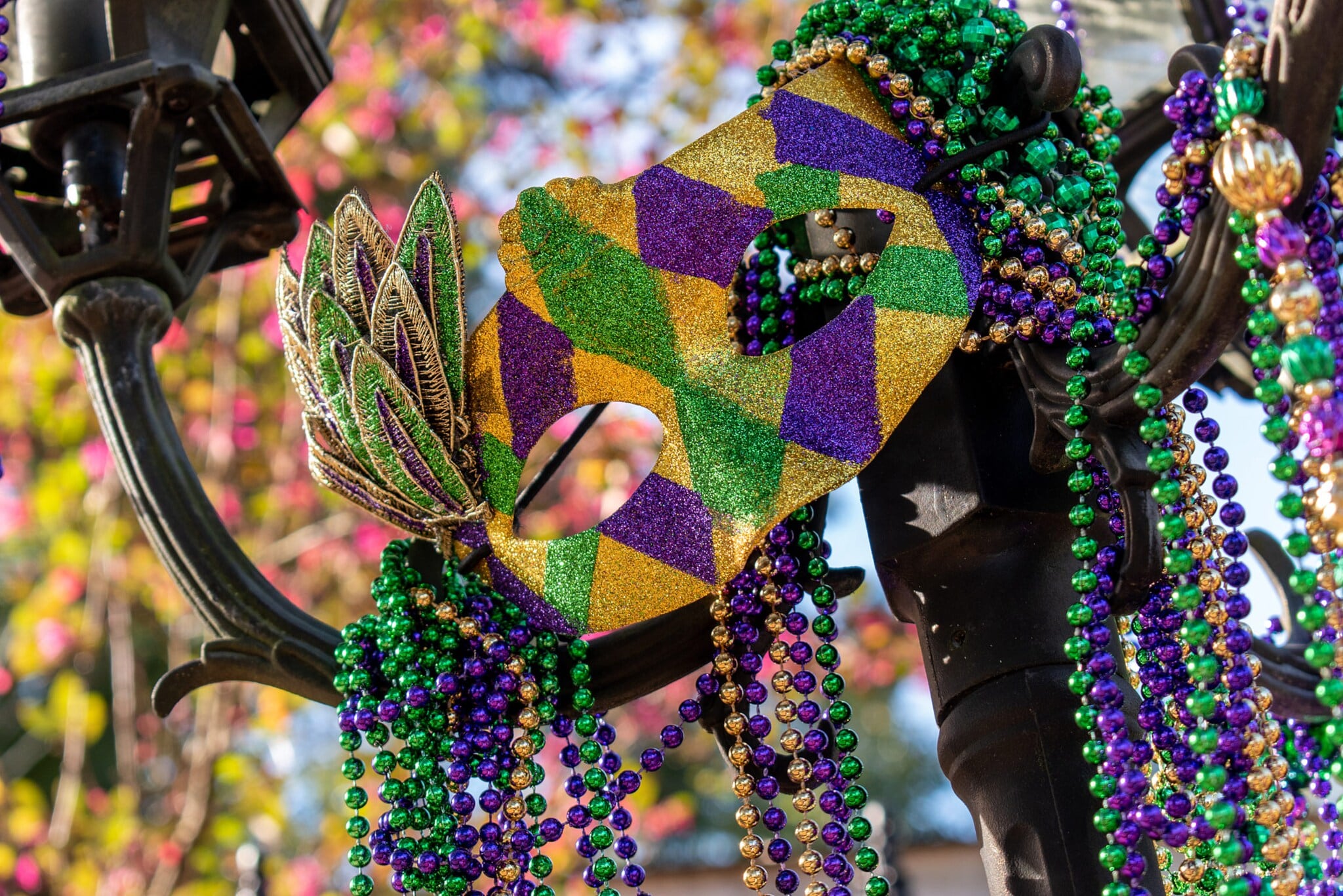 Eine Maske und Perlenketten in den Farben Grün, Gold und Violett an einer Straßenlaterne. Eine Maske und Perlenketten in den Farben Grün, Gold und Violett an einer Straßenlaterne.